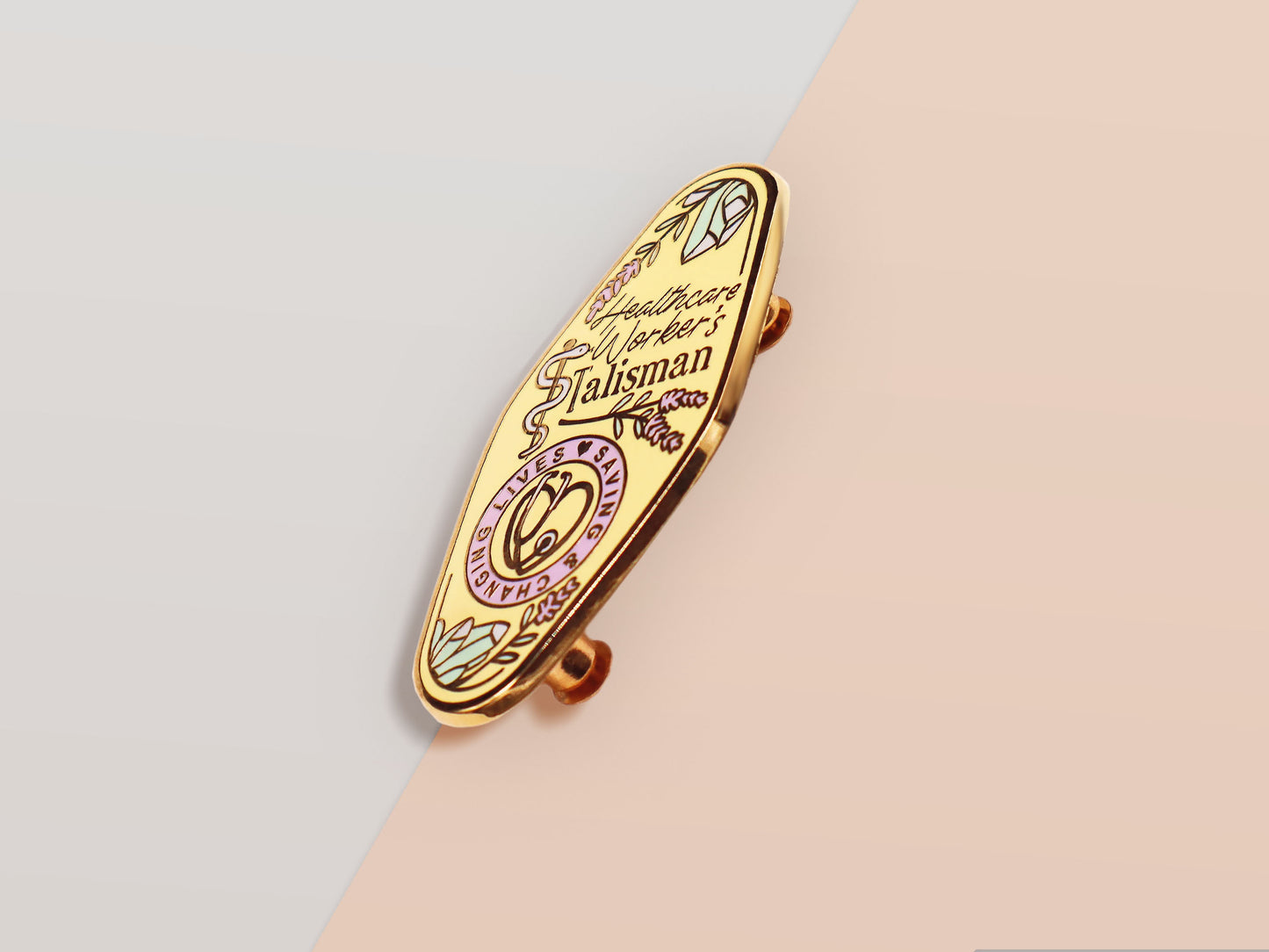 A Health Worker's Talisman gold enamel pin on a gold foiled backing card that outlines the symbolism of the talisman including information and imagery on the Rod of Asclepius, Lavender Stems and Prehnite Crystals