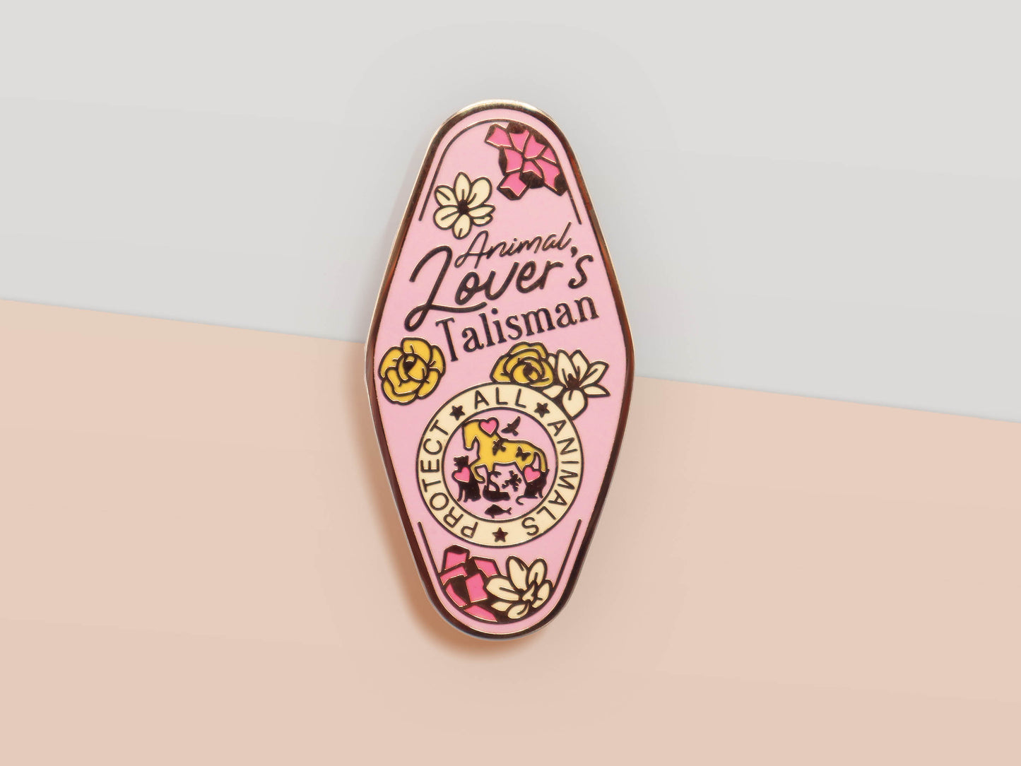 An Animal Lover's Talisman gold enamel pin on a gold foiled backing card that outlines the symbolism of the talisman including information and imagery on Magnolia flowers, yellow roses, and aragonite star clusters