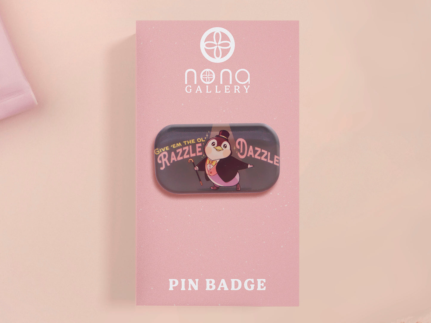 A clear acrylic pin badge with a pink heart-shaped pin back clasp. The design of the pin badge is of a cute chibi penguin dancing in a suit under a spotlight with the quote give 'em the ol' razzle dazzle