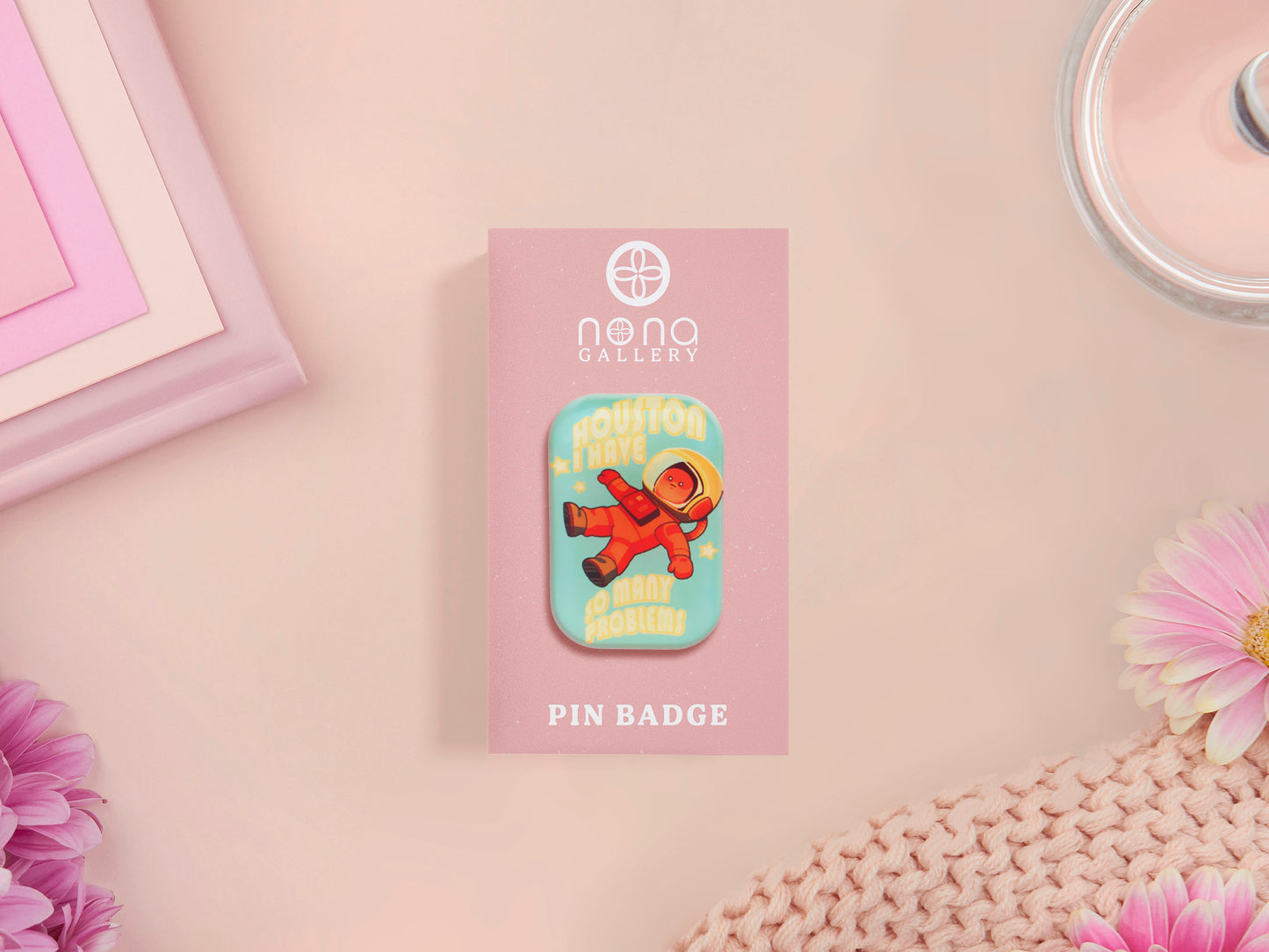 A clear acrylic pin badge with a pink heart-shaped pin back clasp. The design of the pin badge is of a cute chibi retro astronaut floating in sapce with the quote Houston I have so many problems