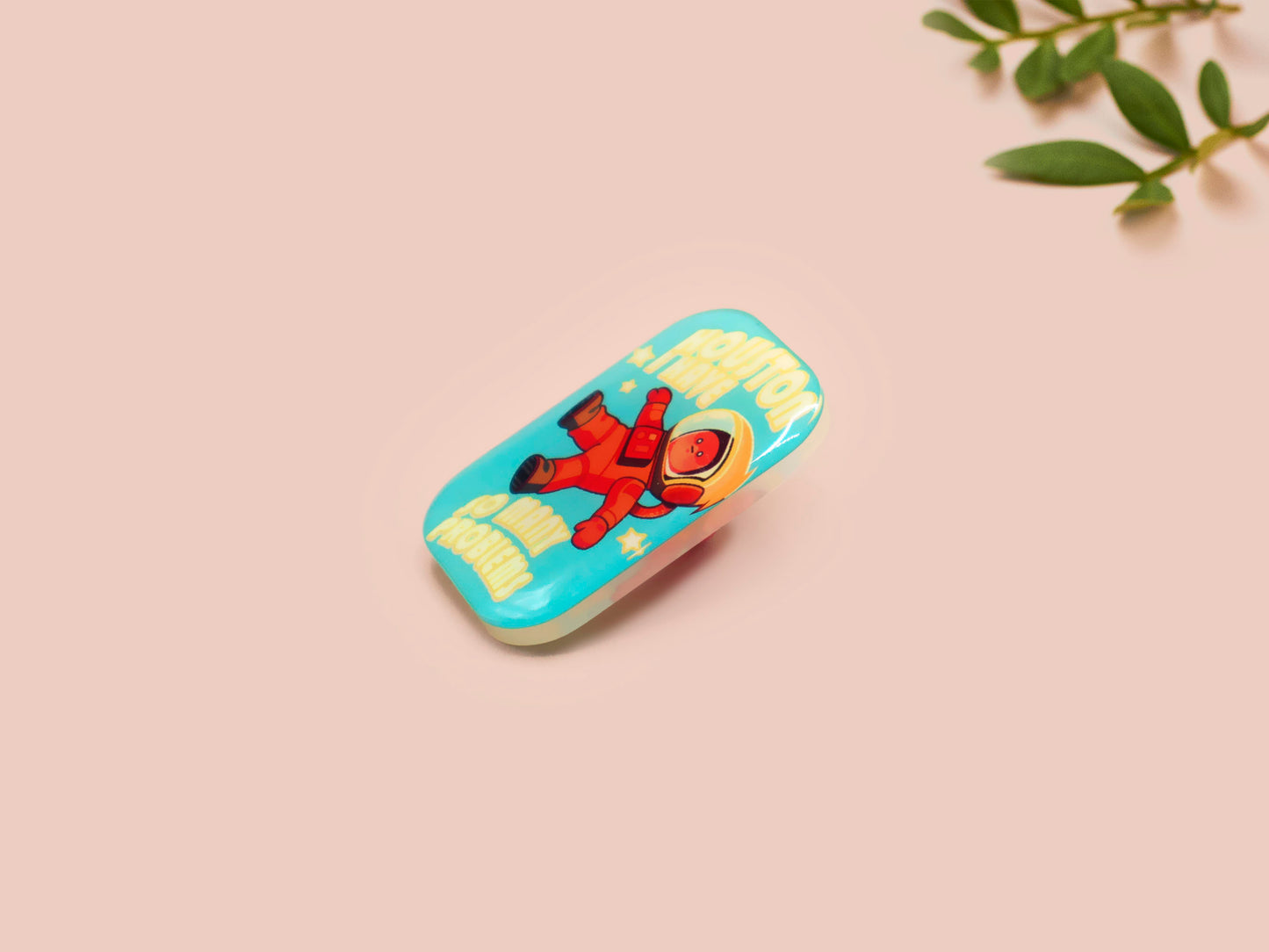 A clear acrylic pin badge with a pink heart-shaped pin back clasp. The design of the pin badge is of a cute chibi retro astronaut floating in sapce with the quote Houston I have so many problems