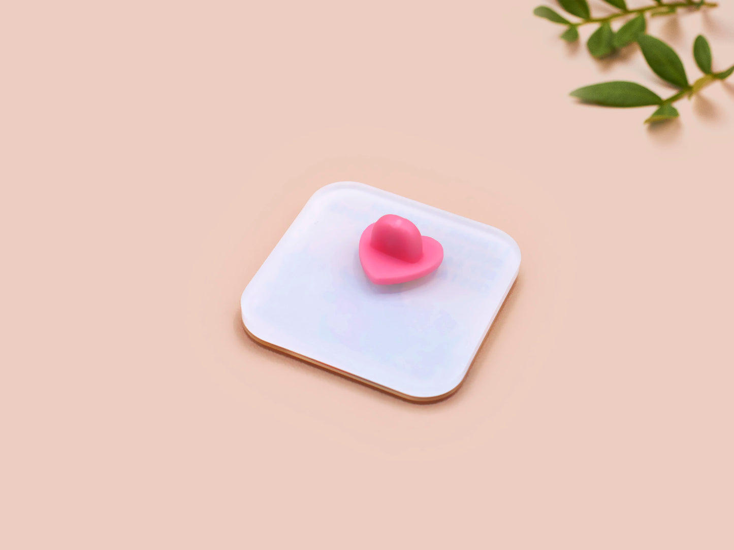 Small pink heart-shaped object on a white square base with a beige background