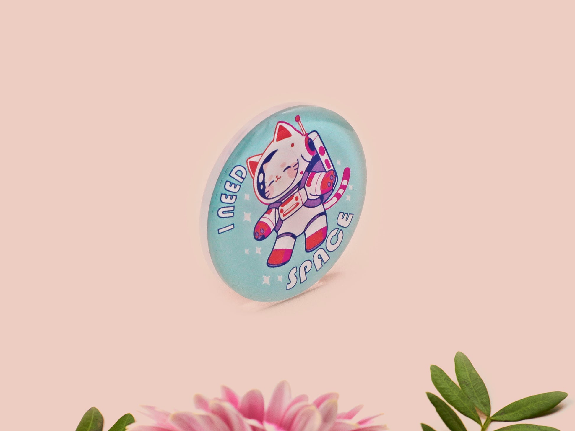 Clear acrylic pin badge with a pink heart-shaped rubber pin back clasp. The design of the pin badge is a cute chibi white cat in a retro astronaut suit with the quote I need space.