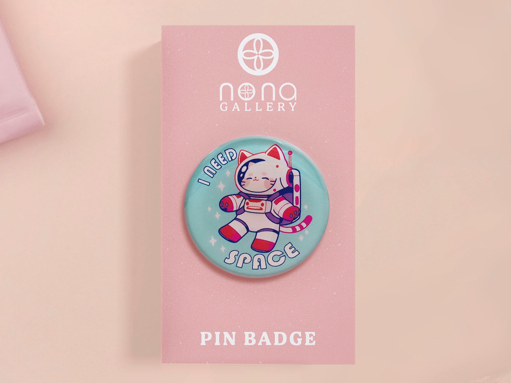 Clear acrylic pin badge with a pink heart-shaped rubber pin back clasp. The design of the pin badge is a cute chibi white cat in a retro astronaut suit with the quote I need space.