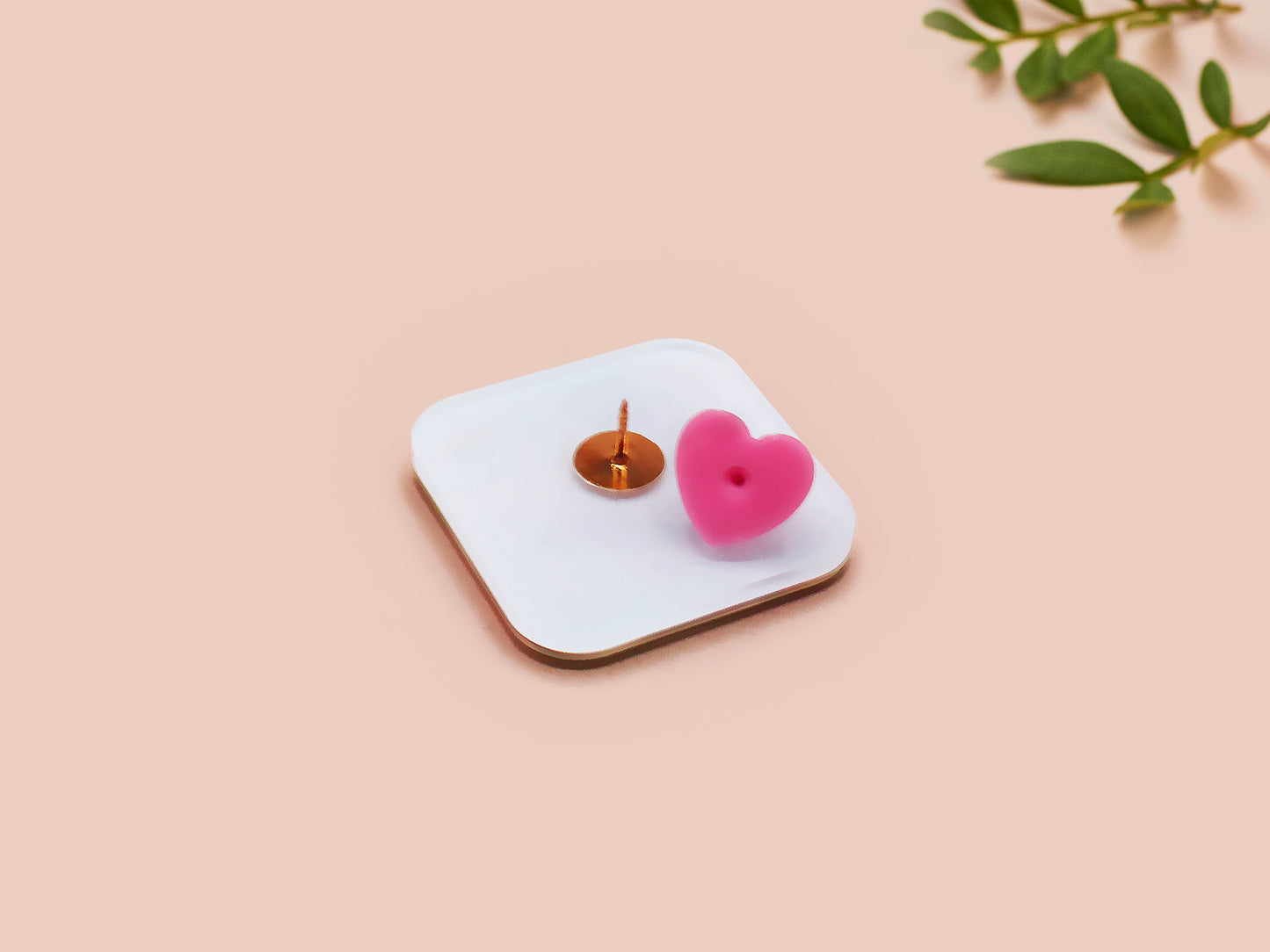 A clear acrylic pin badge with a pink heart-shaped pin back clasp. The design of the pin badge is of a cute chibi pigeon wearing a top hat crying next to a pethetic attempt at nest building with the quote I'm trying my best.