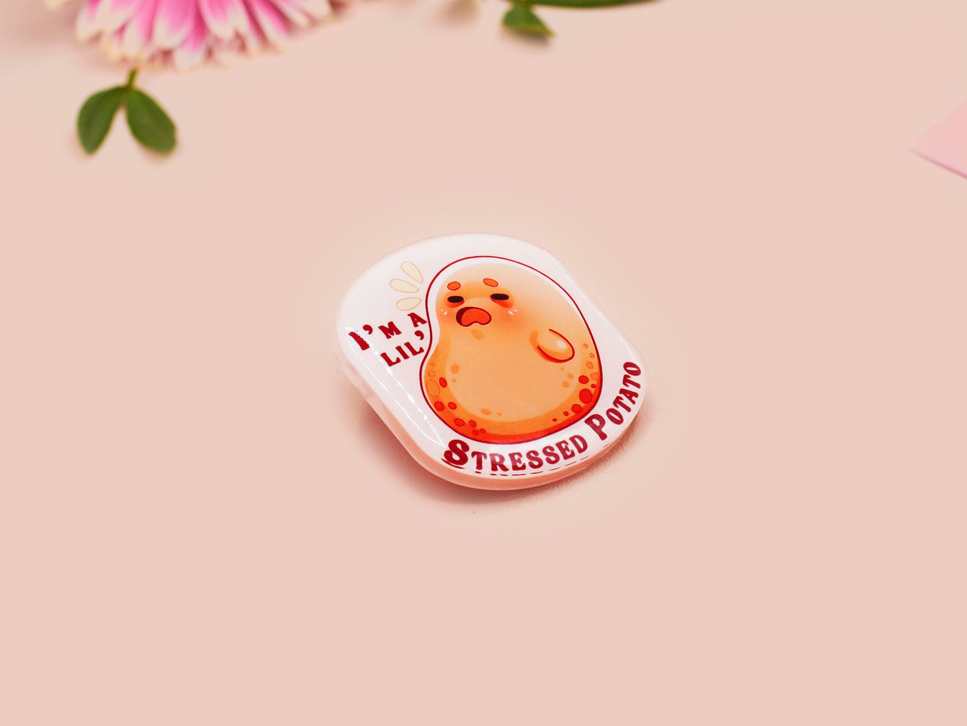 A clear acrylic pin badge with a pink heart-shaped pin back clasp. The design of the pin badge is of a cute chibi potato with the quote I'm a lil' stressed potato