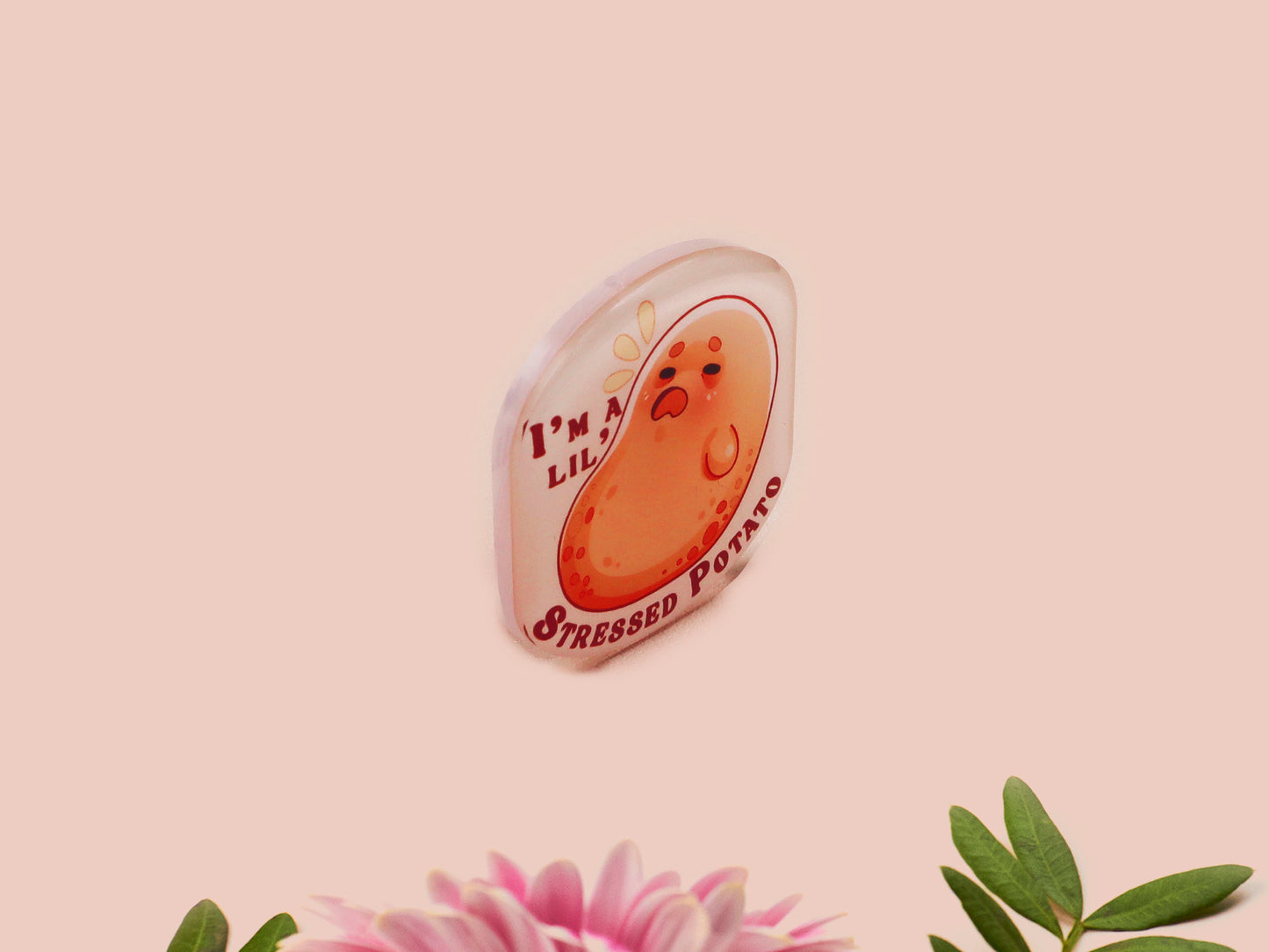 A clear acrylic pin badge with a pink heart-shaped pin back clasp. The design of the pin badge is of a cute chibi potato with the quote I'm a lil' stressed potato