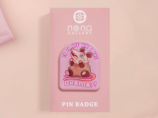 A clear acrylic pin badge with a pink heart-shaped pin back clasp. The design of the pin badge is of a cute screaming possum with the quote is it me am I the drama?
