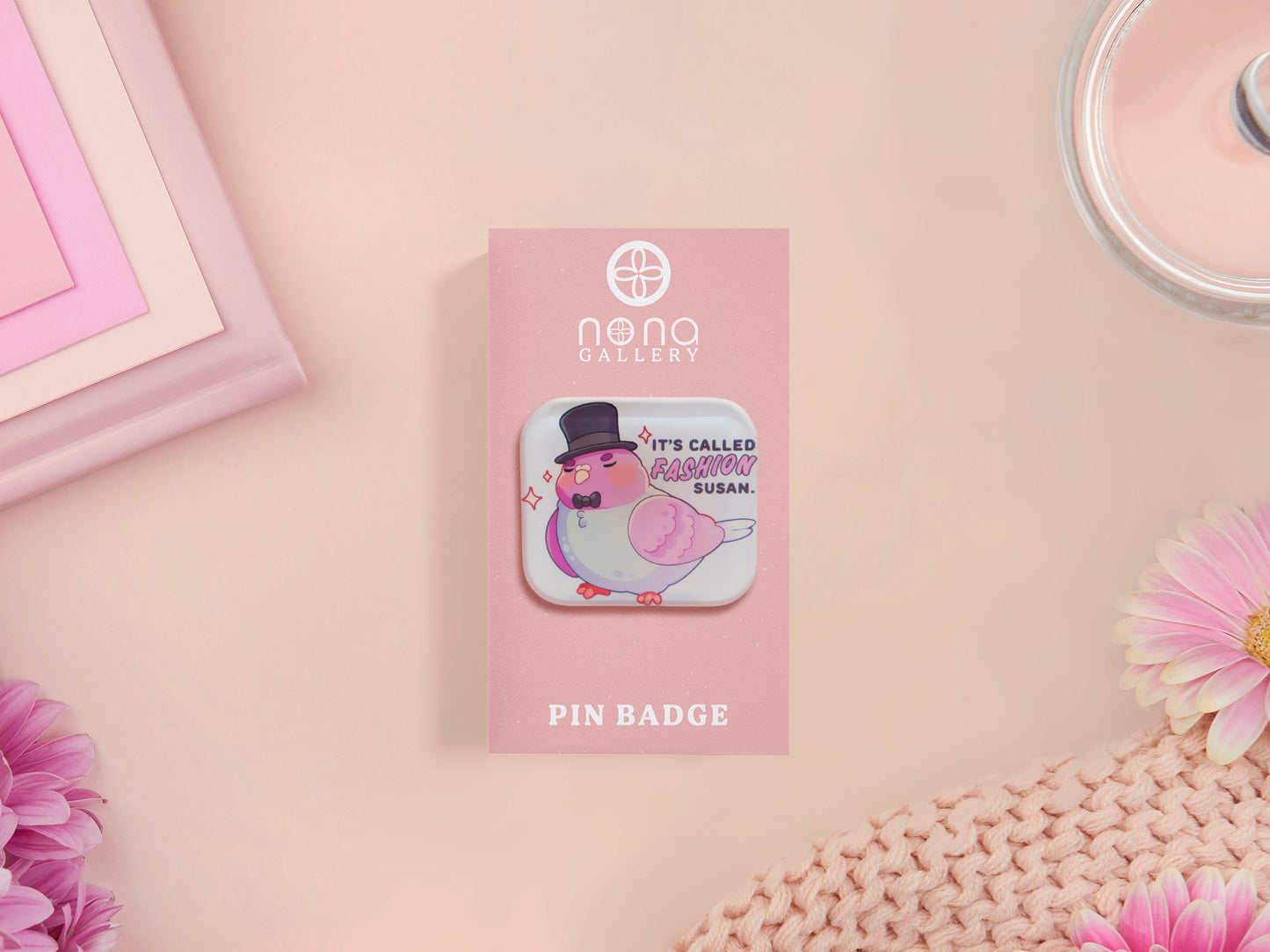 A clear acrylic pin badge with a pink heart-shaped pin back clasp. The design of the pin badge is of a cute chibi pigeon wearing a top hat with the quoteit's called fashion susan