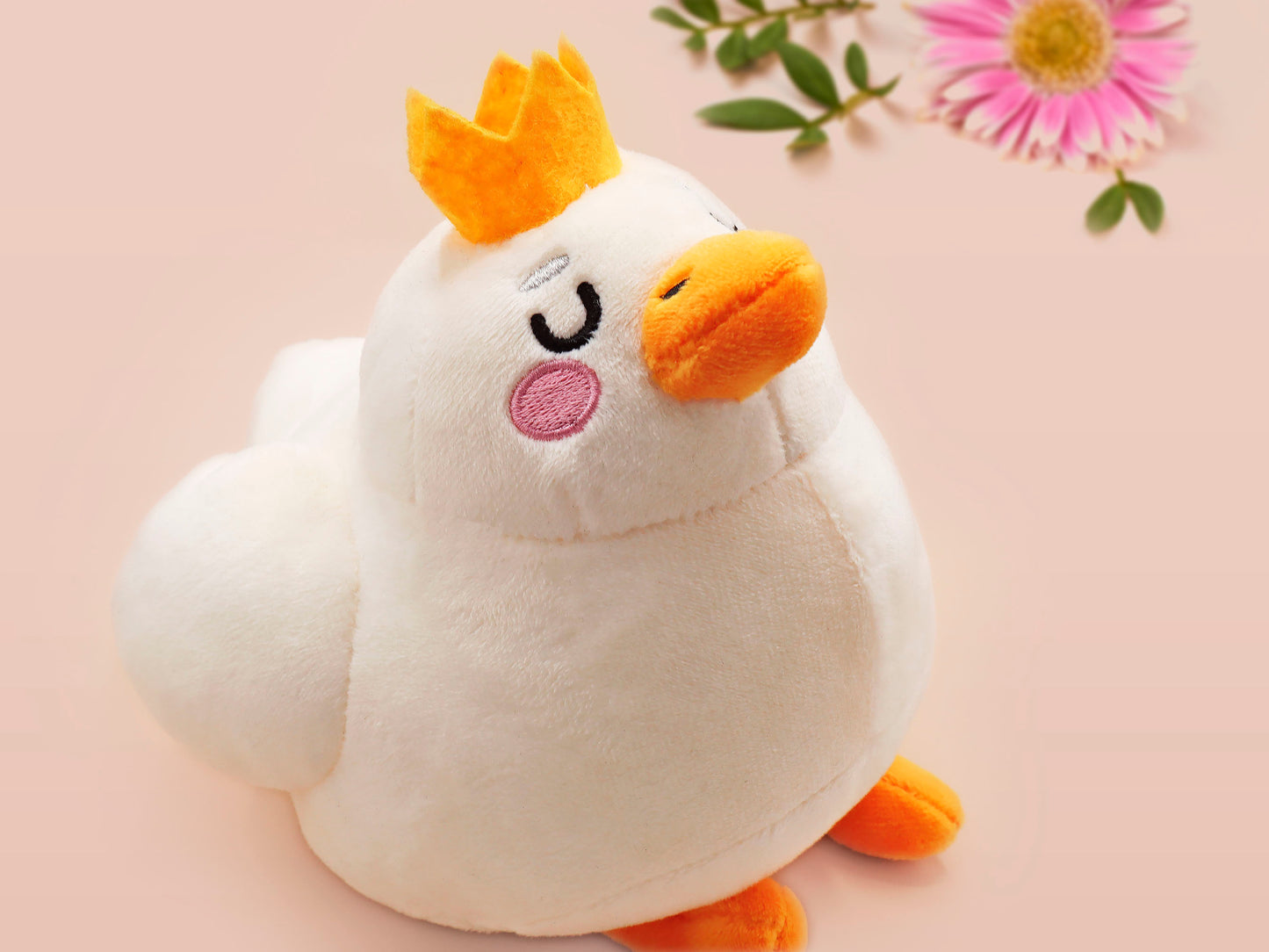 An adorable white duck bird plushie toy with cute embroidered eyes and facial expression, wearing a yellow crown hat, with a hang tag describing the duck as King Larry.