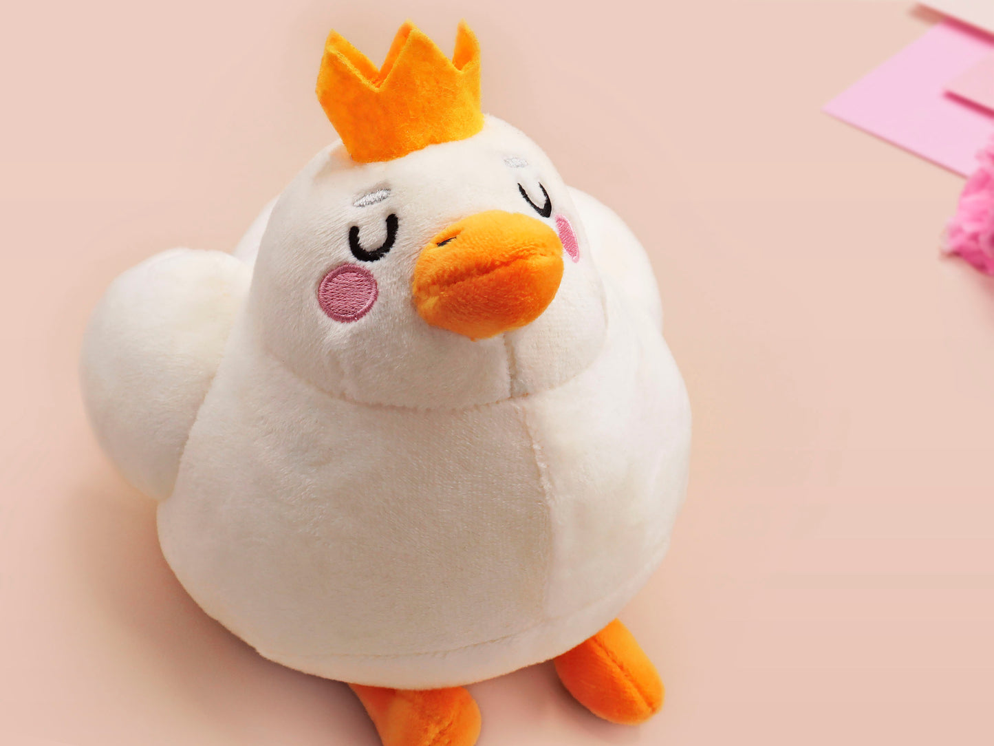 An adorable white duck bird plushie toy with cute embroidered eyes and facial expression, wearing a yellow crown hat, with a hang tag describing the duck as King Larry.