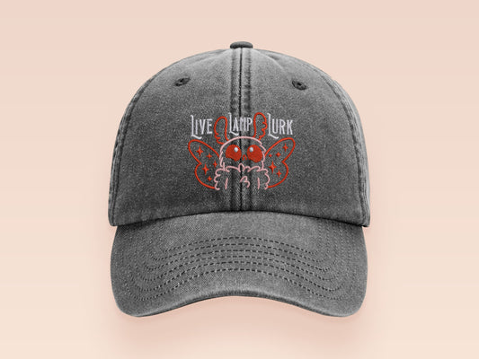 A vintage dark grey baseball cap hat with an embroidered cute chibi Mothman crytid with the quote Live Lamp Lurk.