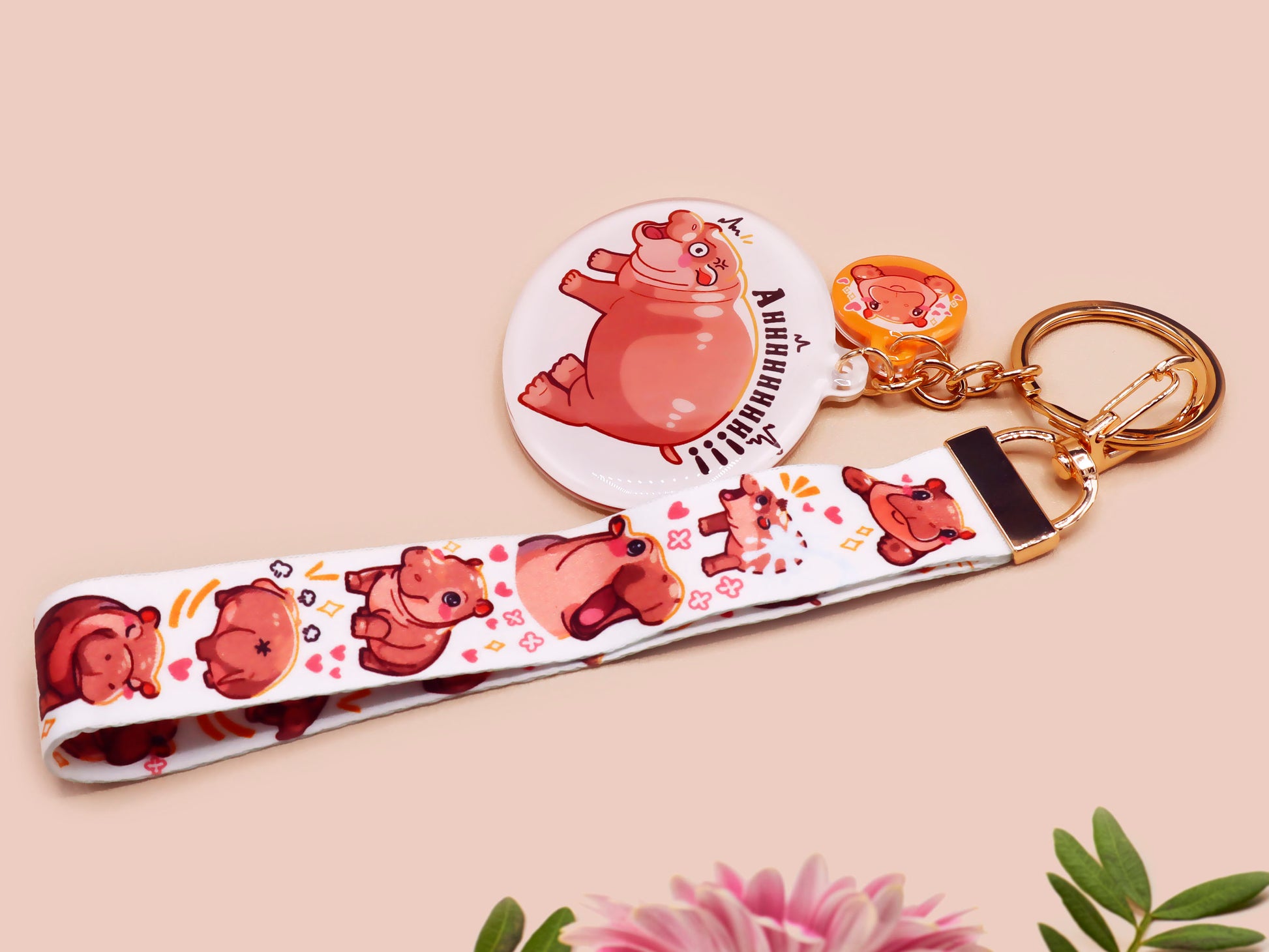 Acrylic keychain with a large charm of the fat angry pygmy hippo being picked up, a smaller charm of a cute baby hippo with the name Moo Deng in Thai and a matching mini lanyard of the pygmy hippo in multiple cute poses and expressions.