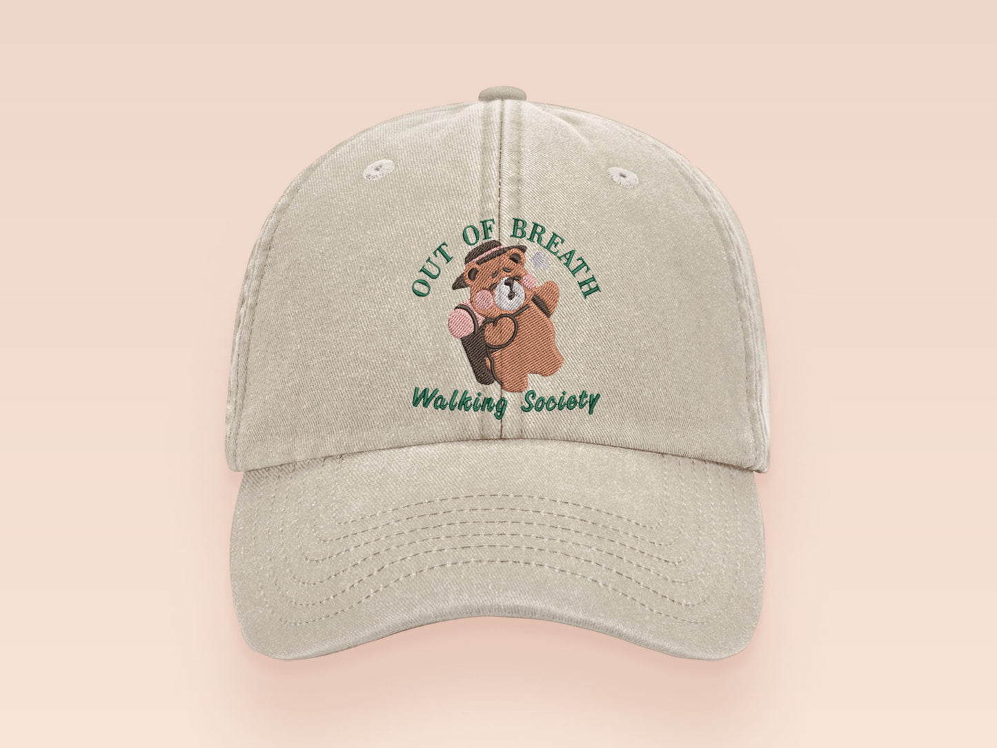 A cream baseball cap hat with an embroidered cute brown bear hiking with the quote out of breath walking society.