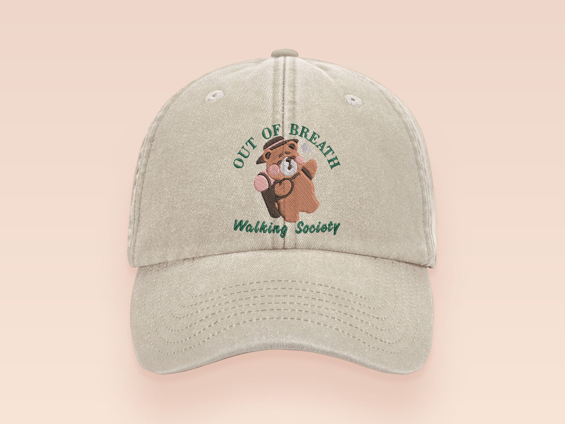 A cream baseball cap hat with an embroidered cute brown bear hiking with the quote out of breath walking society.