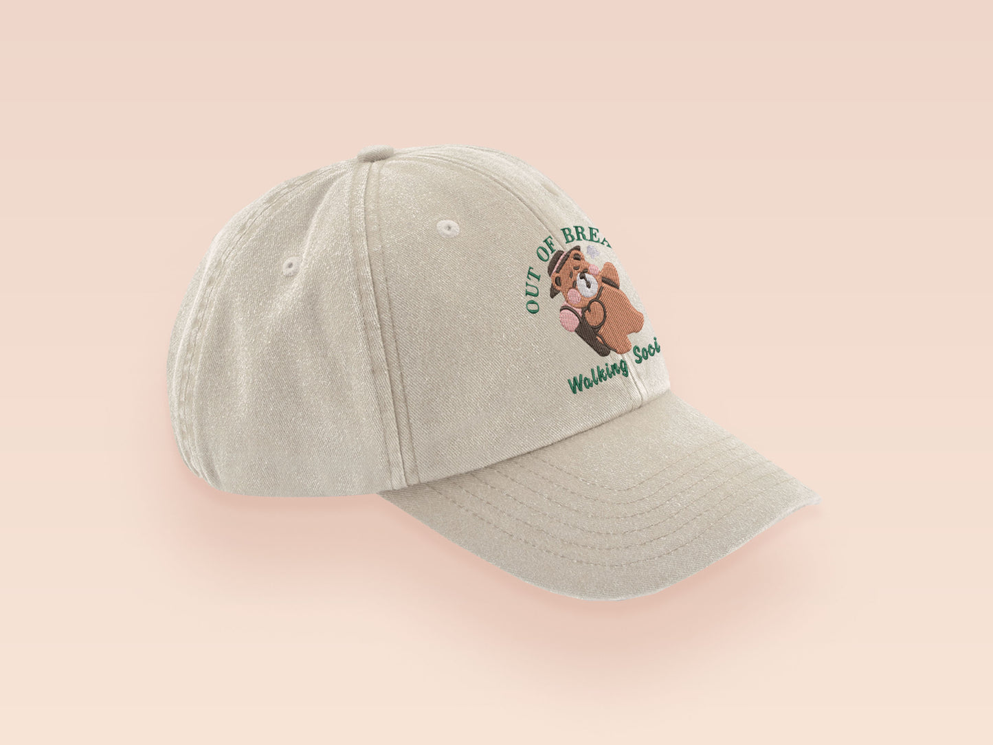 A cream baseball cap hat with an embroidered cute brown bear hiking with the quote out of breath walking society.