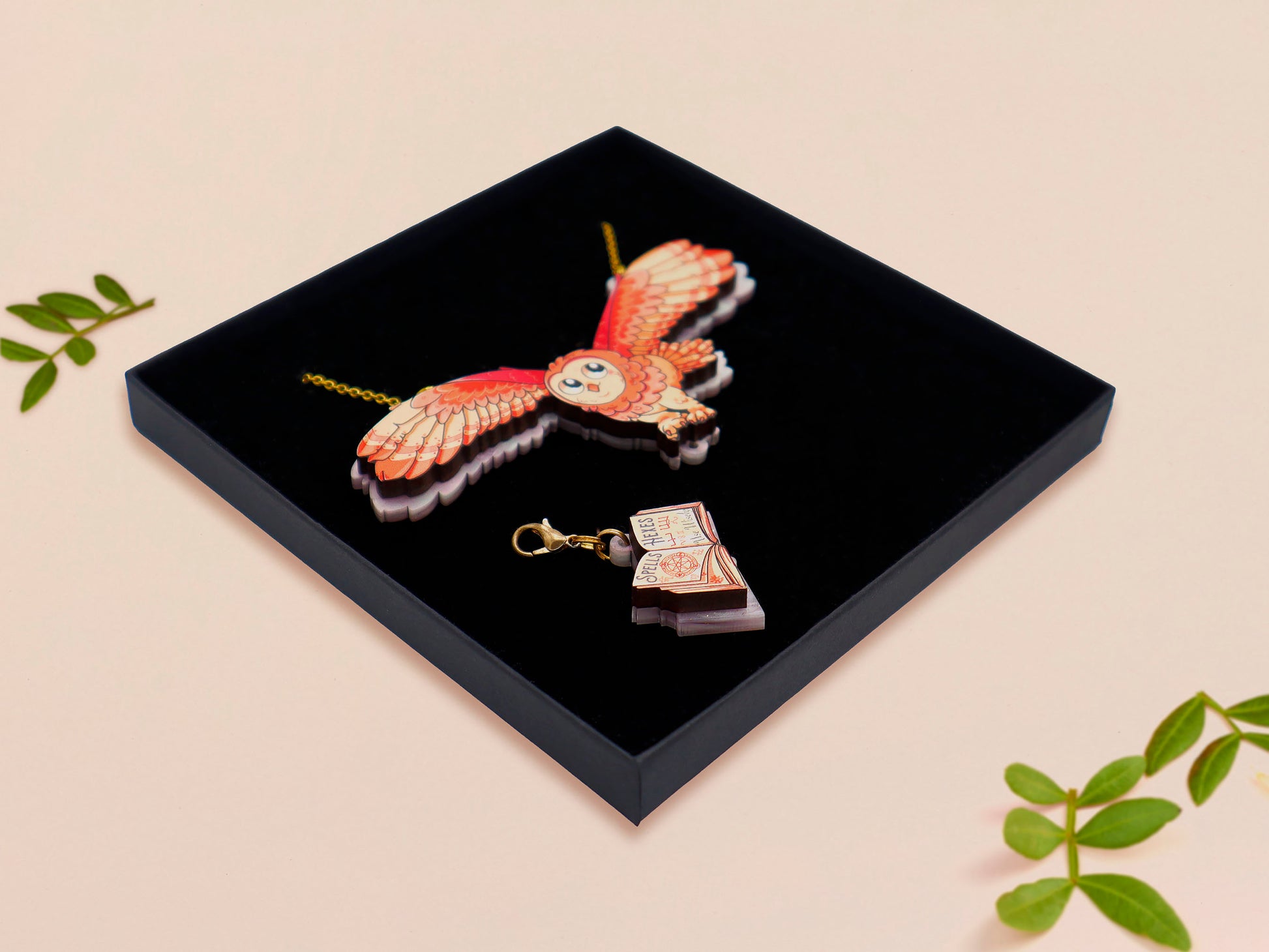 Mixed material handmade necklace of chibi cartoon flying barn owl with pearlescent wings carrying a removeable spell book charm, with a gold chain and black gift box.