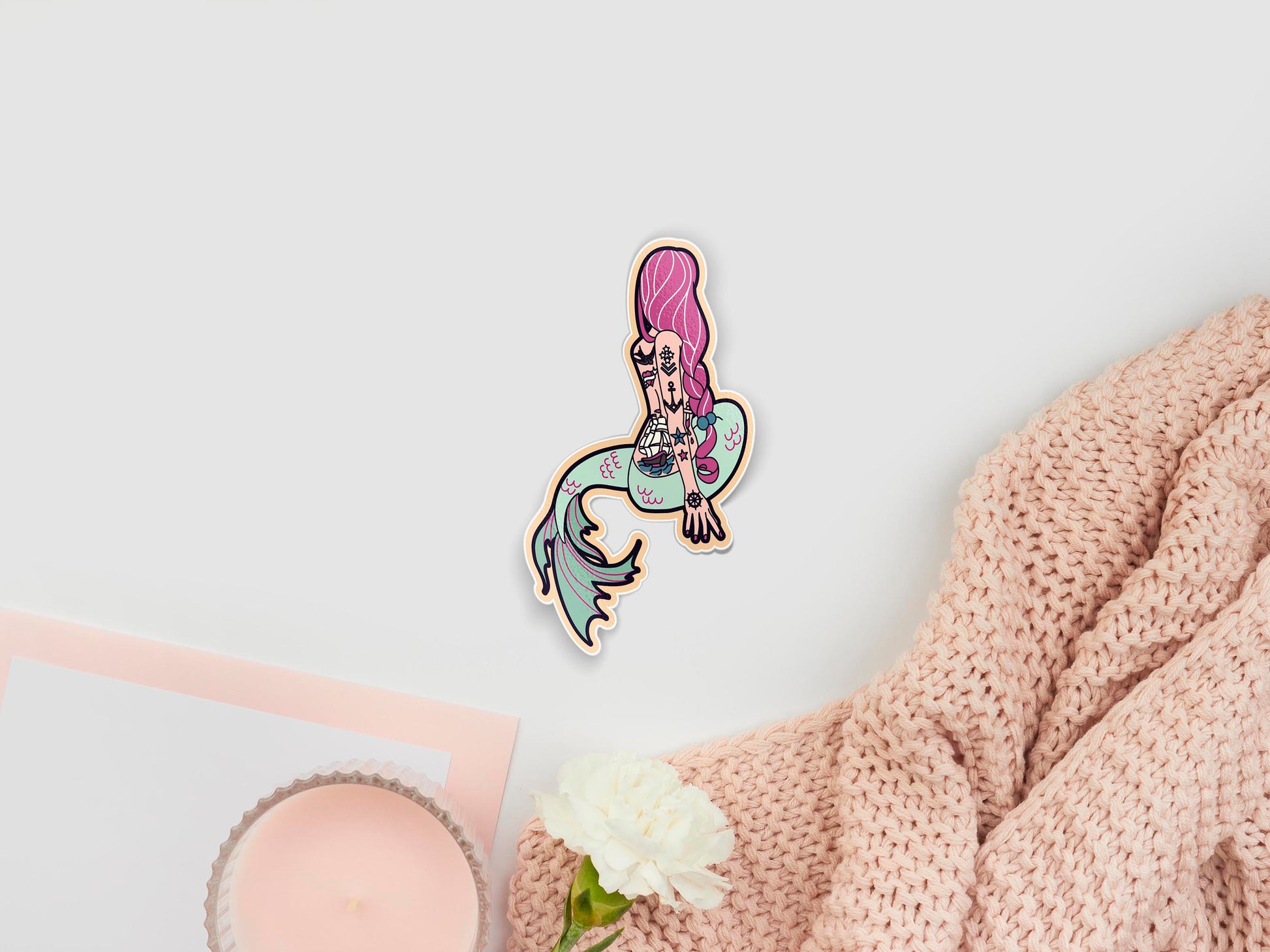 Large sticker sheet of digital illustration cartoons of a mermaid sat facing away, with long pink hair, a pale green tale and a back and arm filled with nautical tattoos, such as a tall ship and anchor