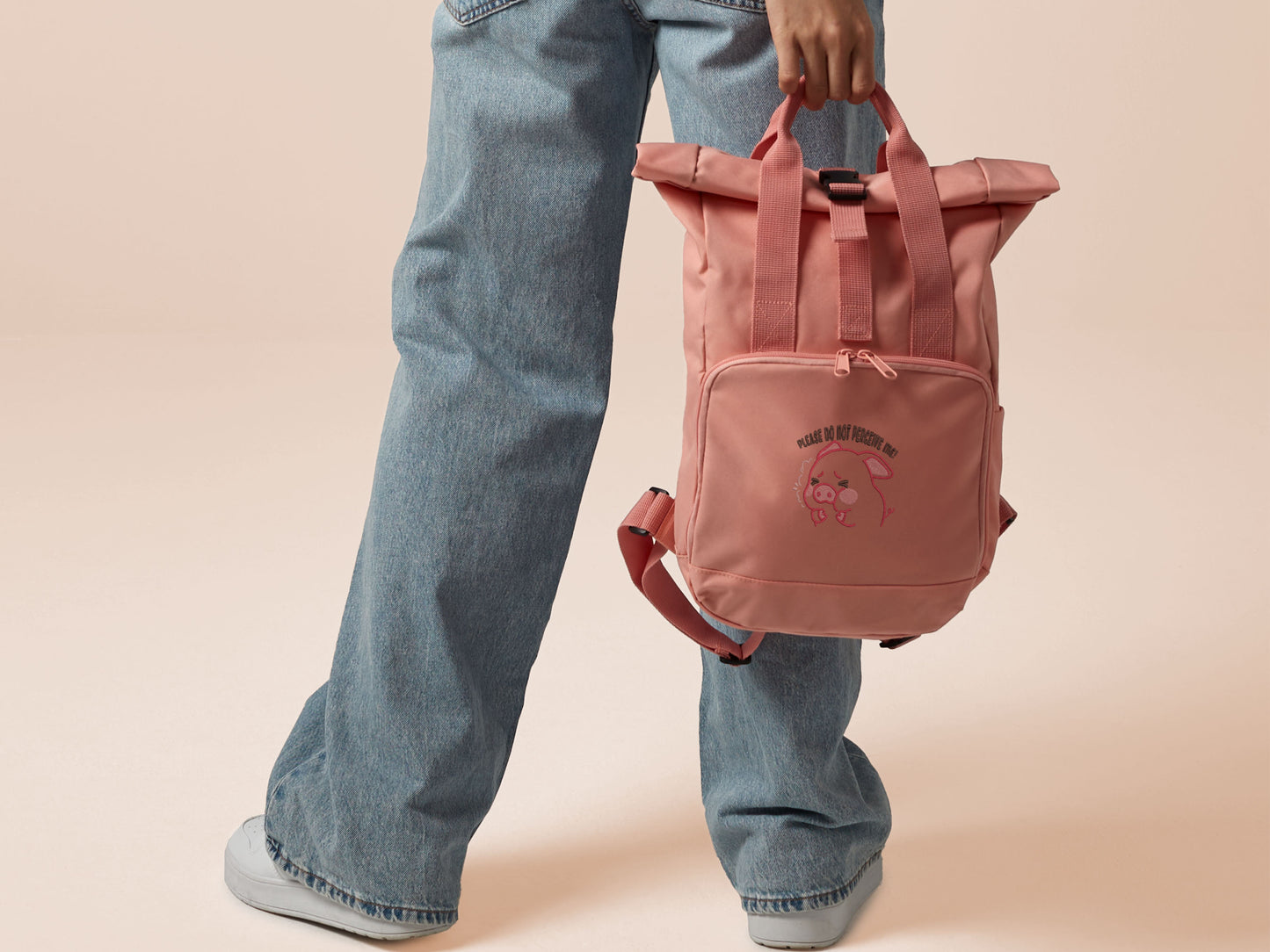 Pink roll top twin handle backpack with an embroided design of cute crying pig and the quote please do not percive me
