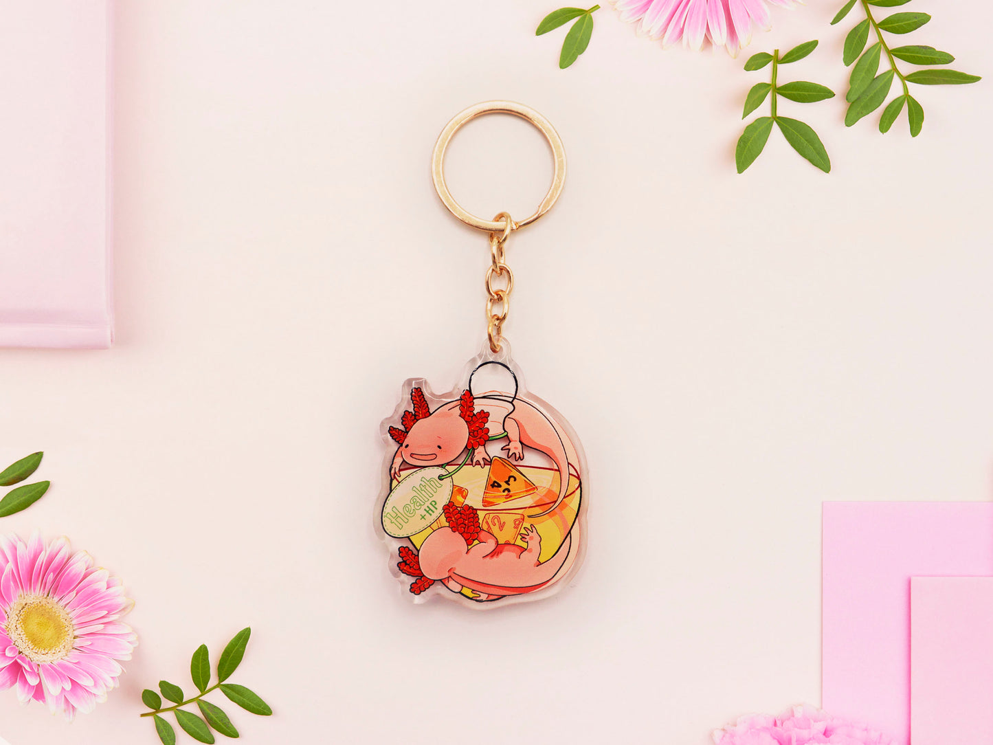 Clear acrylic double sided gold clasp keychain with a cartoon illustrated design of two pink axolotls on a potion bottle labelled health +hp and with a yellow liquid and four orange d4 dice inside.