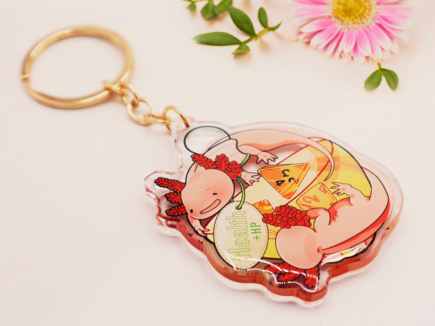 Clear acrylic double sided gold clasp keychain with a cartoon illustrated design of two pink axolotls on a potion bottle labelled health +hp and with a yellow liquid and four orange d4 dice inside.