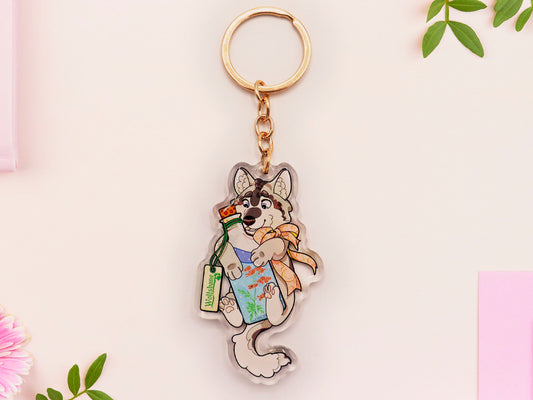 Clear acrylic keychain with gold clasp with a cartoon illustration of a wolf husky dog with a bow hugging a potion bottle with a blue liquid and wolfsbane flower inside, labelled wolfsbane.
