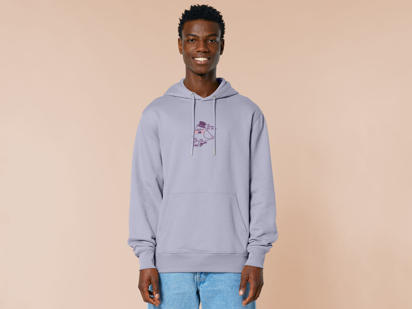 An embroidered purple hoodie design of a cute pigeon wearing a top hat building a pathetic nest and the text I'm trying my best.