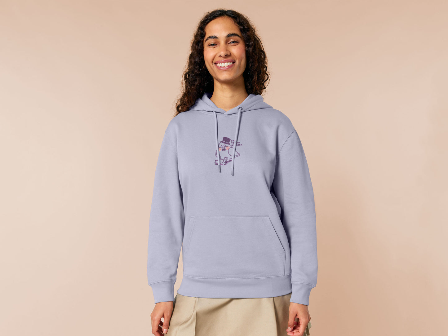 An embroidered purple hoodie design of a cute pigeon wearing a top hat building a pathetic nest and the text I'm trying my best.
