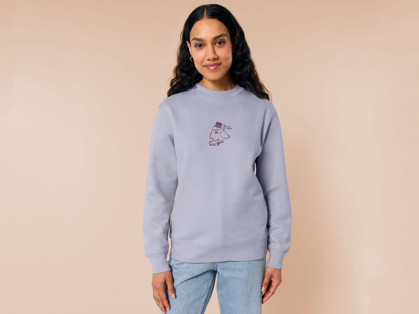 An embroidered purple sweater design of a cute pigeon wearing a top hat building a pathetic nest and the text I'm trying my best.