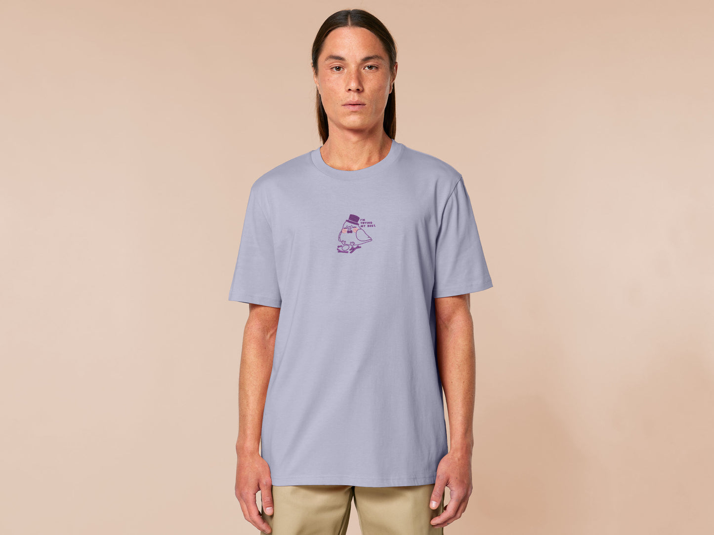 An embroidered purple t-shirt design of a cute pigeon wearing a top hat building a pathetic nest and the text I'm trying my best.