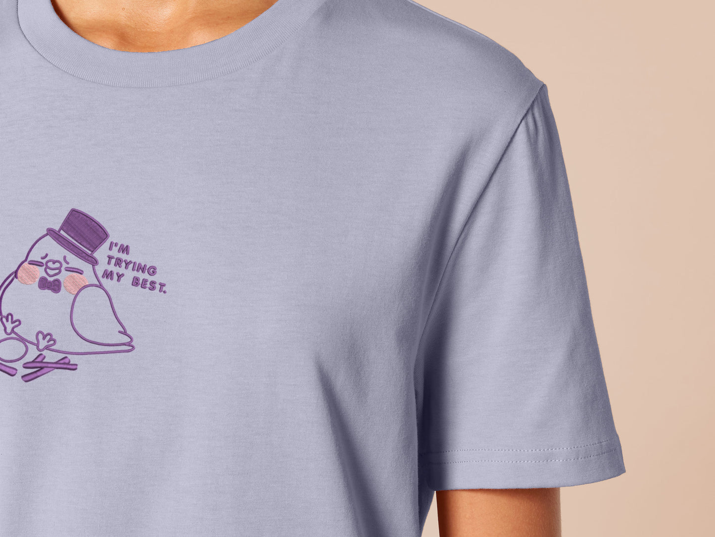 An embroidered purple t-shirt design of a cute pigeon wearing a top hat building a pathetic nest and the text I'm trying my best.