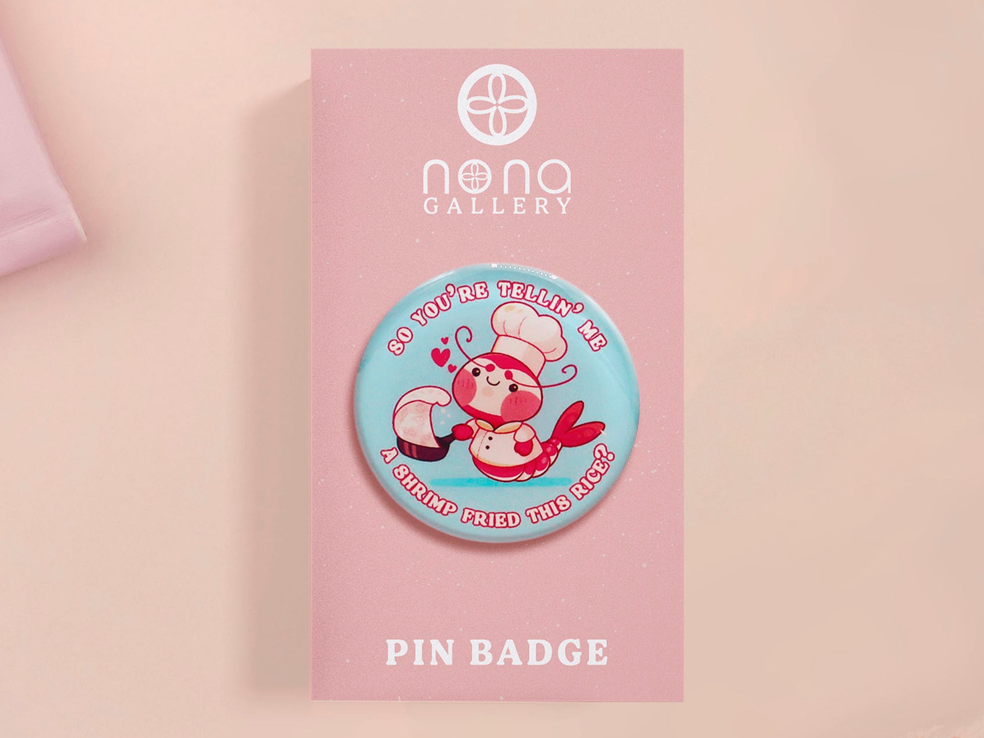 A clear acrylic pin badge with a pink heart-shaped pin back clasp. The design of the pin badge is of a cute chibi shrimp in a chefs outfit cooking with the quote So you're telling me a shrimp fried this rice?