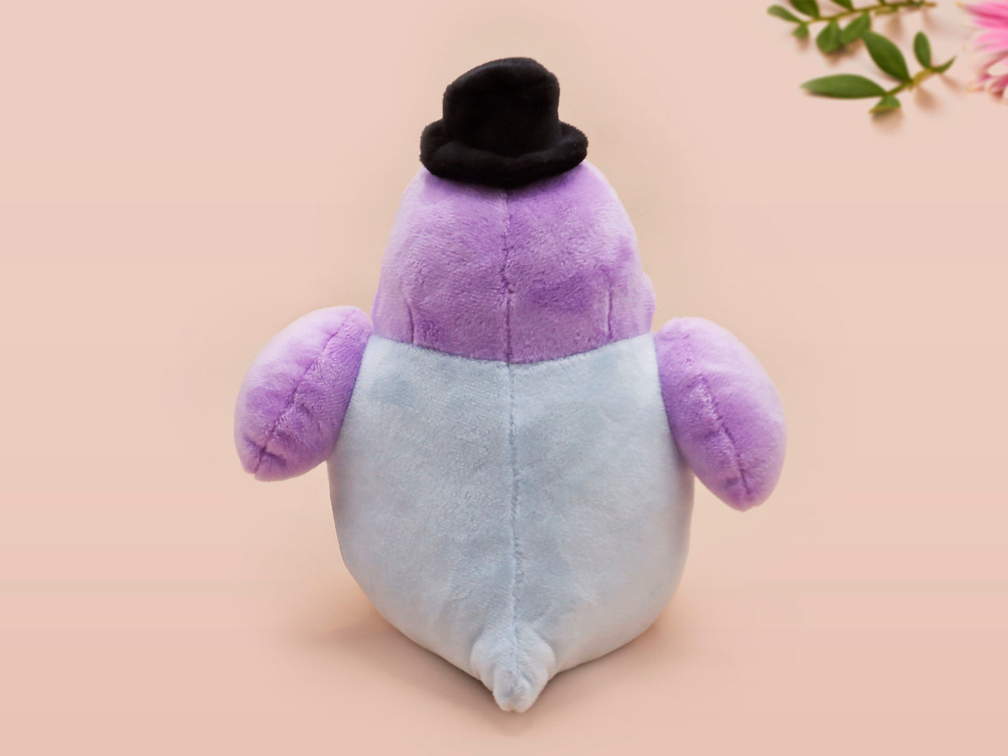 An adorable purple and blue pigeon bird plushie toy with cute embroidered eyes and facial expression, wearing a black top hat and bow tie, with a hang tag describing the pigeon as Susan.