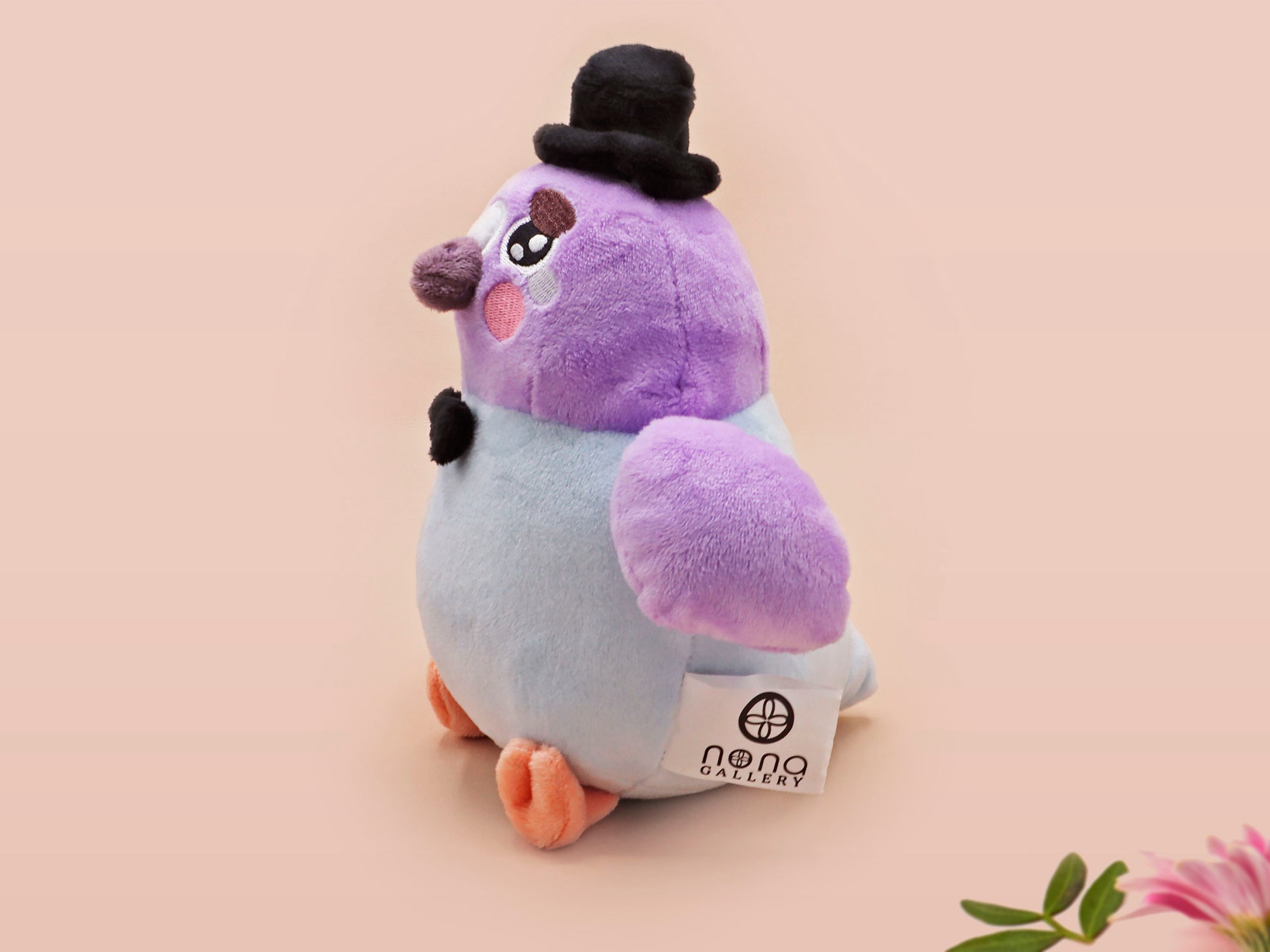 An adorable purple and blue pigeon bird plushie toy with cute embroidered eyes and facial expression, wearing a black top hat and bow tie, with a hang tag describing the pigeon as Susan.