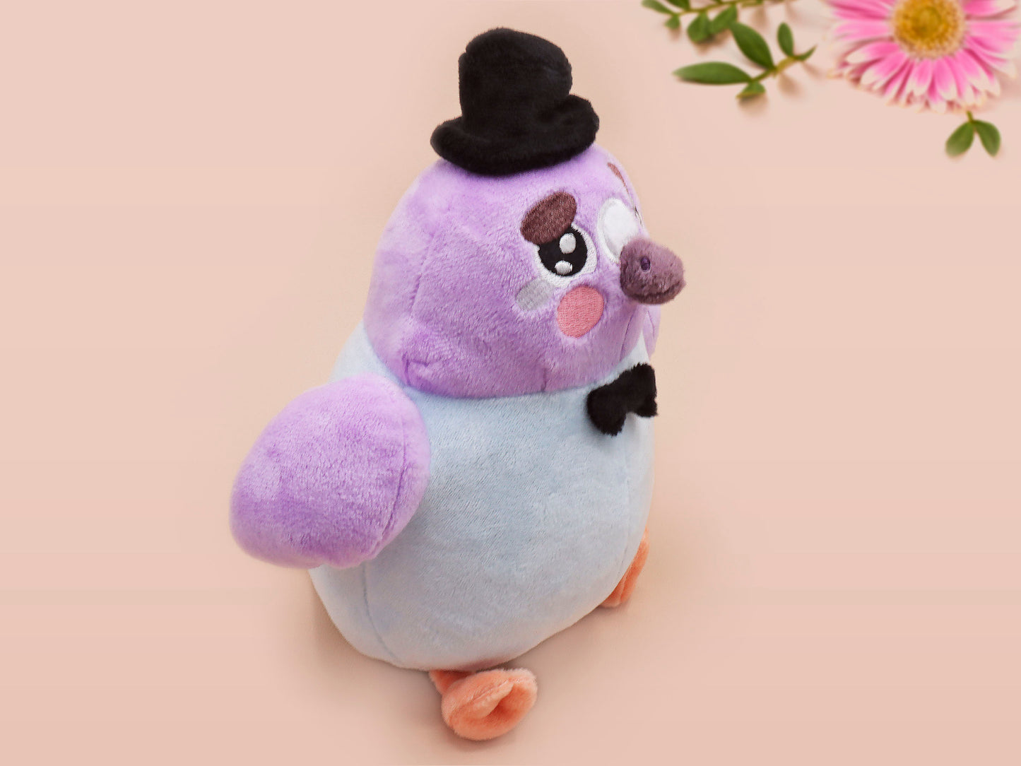 An adorable purple and blue pigeon bird plushie toy with cute embroidered eyes and facial expression, wearing a black top hat and bow tie, with a hang tag describing the pigeon as Susan.