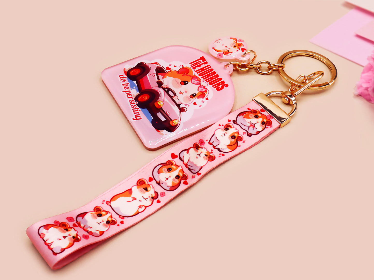 Cute pink keychain and lanyard of an adorable chibi hamster guinea pig in heart sunglasses driving a little pink car with the quote the Horrors do be persisting, with matching mini charm and lanyard of multiple cute fat guinea pig hamsters