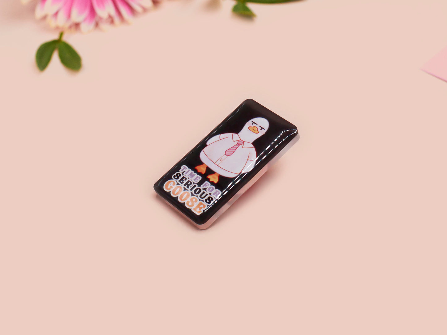 A black acrylic pin badge with a pink heart-shaped pin back clasp. The design of the pin badge is of a cute goose in a shirt and tie with the quote Time For Serious Goose