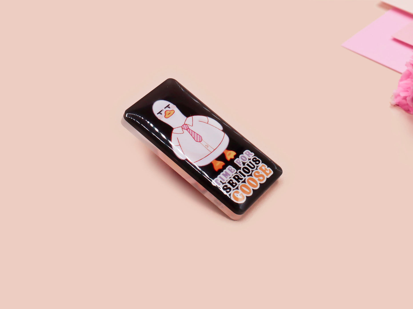 A black acrylic pin badge with a pink heart-shaped pin back clasp. The design of the pin badge is of a cute goose in a shirt and tie with the quote Time For Serious Goose