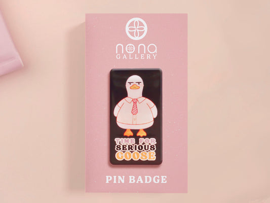 A black acrylic pin badge with a pink heart-shaped pin back clasp. The design of the pin badge is of a cute goose in a shirt and tie with the quote Time For Serious Goose
