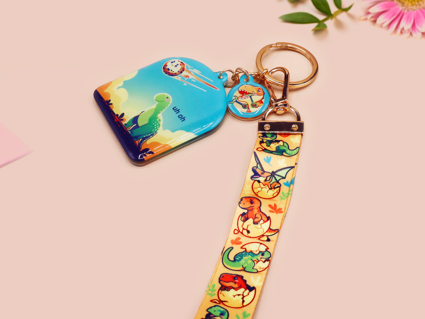 Acrylic epoxy dinosaur keychain with a large acrylic charm of a long necked dinosaur looking up at an incoming asteroid with the quote uh oh, a smaller charm of a cute trex with arm grabbers and a matching hatching baby dinosaur lanyard.