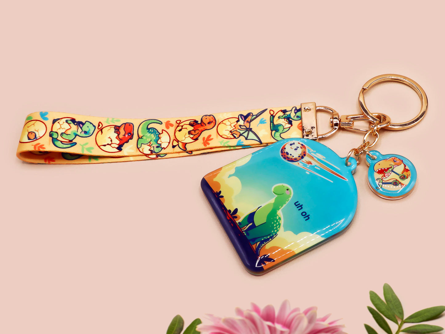 Acrylic epoxy dinosaur keychain with a large acrylic charm of a long necked dinosaur looking up at an incoming asteroid with the quote uh oh, a smaller charm of a cute trex with arm grabbers and a matching hatching baby dinosaur lanyard.