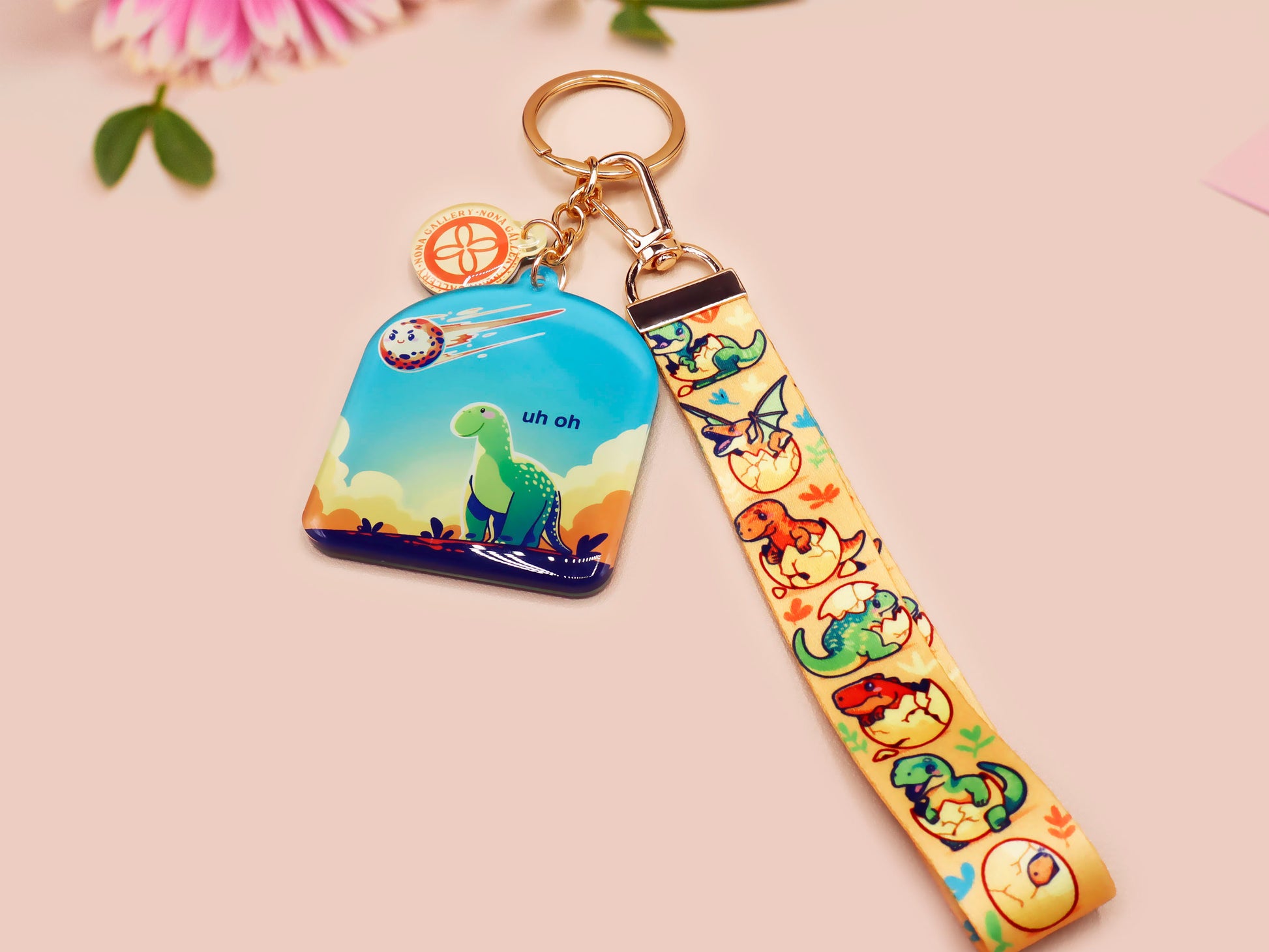 Acrylic epoxy dinosaur keychain with a large acrylic charm of a long necked dinosaur looking up at an incoming asteroid with the quote uh oh, a smaller charm of a cute trex with arm grabbers and a matching hatching baby dinosaur lanyard.