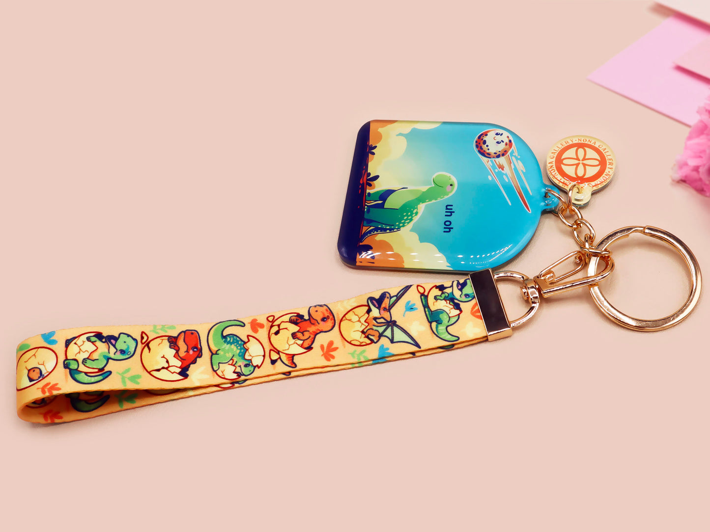 Acrylic epoxy dinosaur keychain with a large acrylic charm of a long necked dinosaur looking up at an incoming asteroid with the quote uh oh, a smaller charm of a cute trex with arm grabbers and a matching hatching baby dinosaur lanyard.
