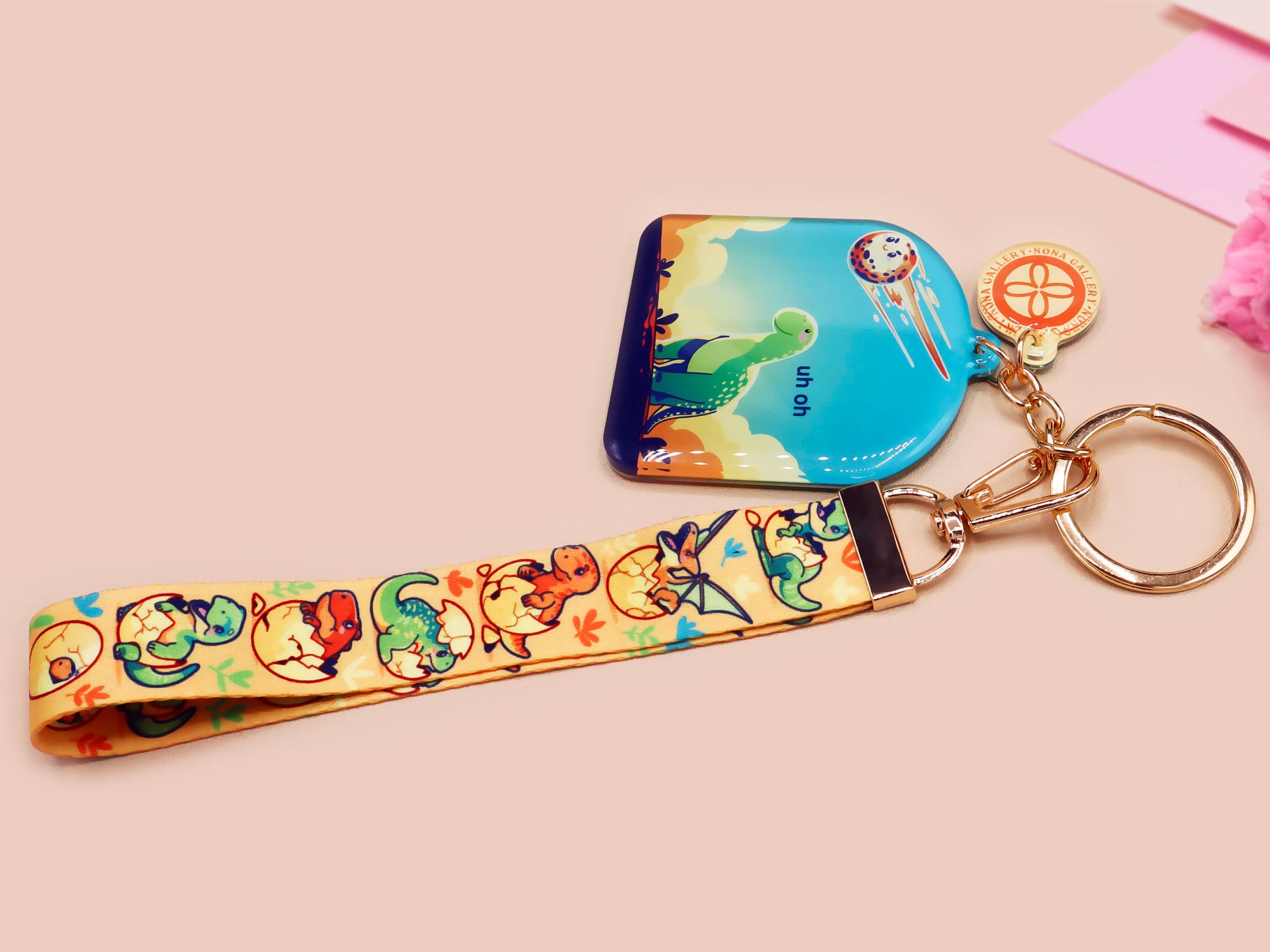 Acrylic epoxy dinosaur keychain with a large acrylic charm of a long necked dinosaur looking up at an incoming asteroid with the quote uh oh, a smaller charm of a cute trex with arm grabbers and a matching hatching baby dinosaur lanyard.