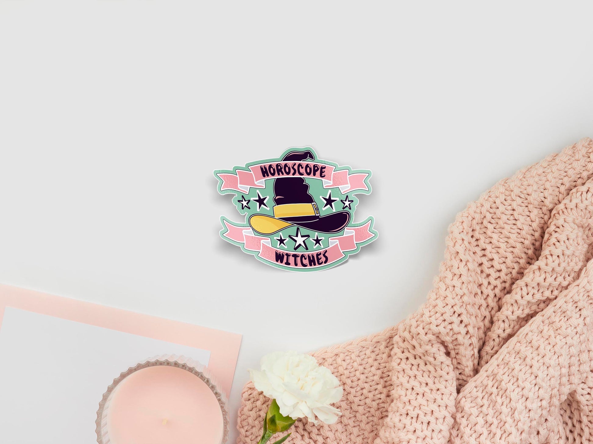 Large sticker of digital illustration cartoon of a dark purple witches hat with a yellow ribbon and buckle, surrounded by stars and two pink ribbons that have the quote Horoscope Witches written on them