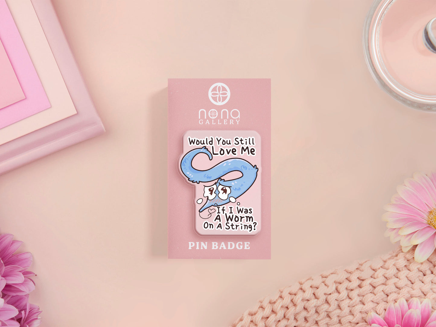 A clear acrylic pin badge with a pink heart-shaped rubber pin back clasp. The pin badge has a design of a cute blue crying worm on a string with the quote would you still love me if I was a worm on a string?
