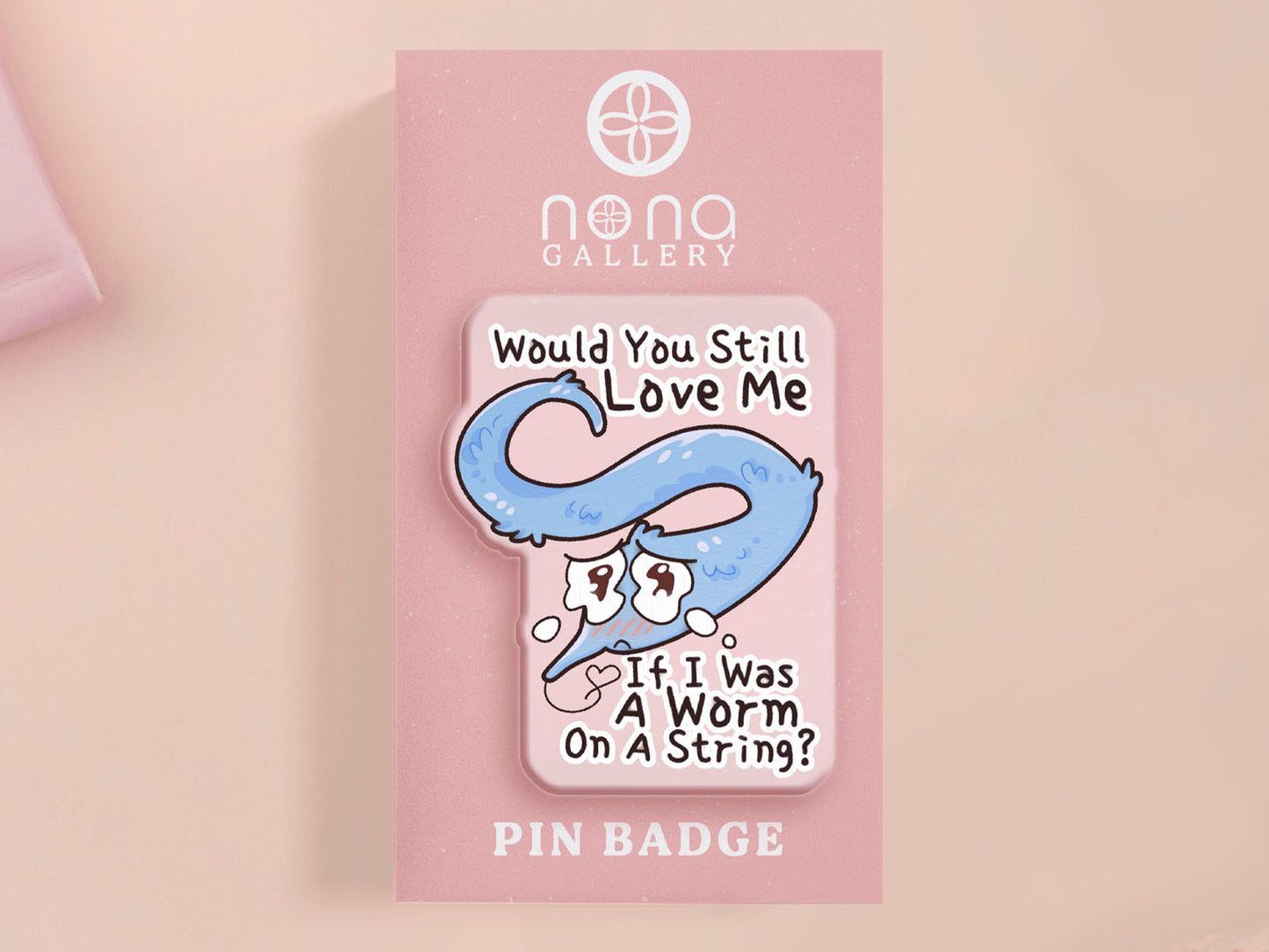 A clear acrylic pin badge with a pink heart-shaped rubber pin back clasp. The pin badge has a design of a cute blue crying worm on a string with the quote would you still love me if I was a worm on a string?