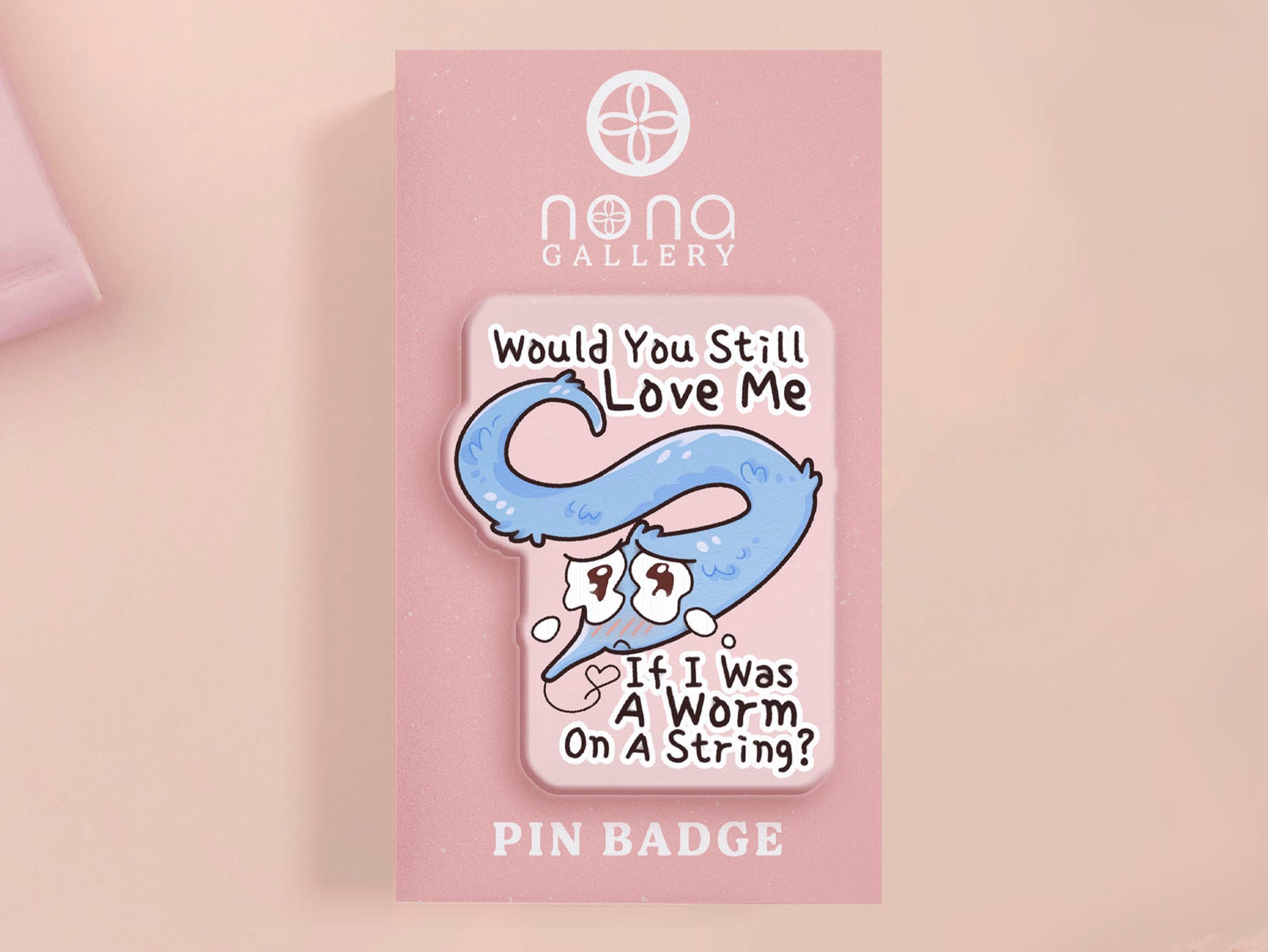 A clear acrylic pin badge with a pink heart-shaped rubber pin back clasp. The pin badge has a design of a cute blue crying worm on a string with the quote would you still love me if I was a worm on a string?