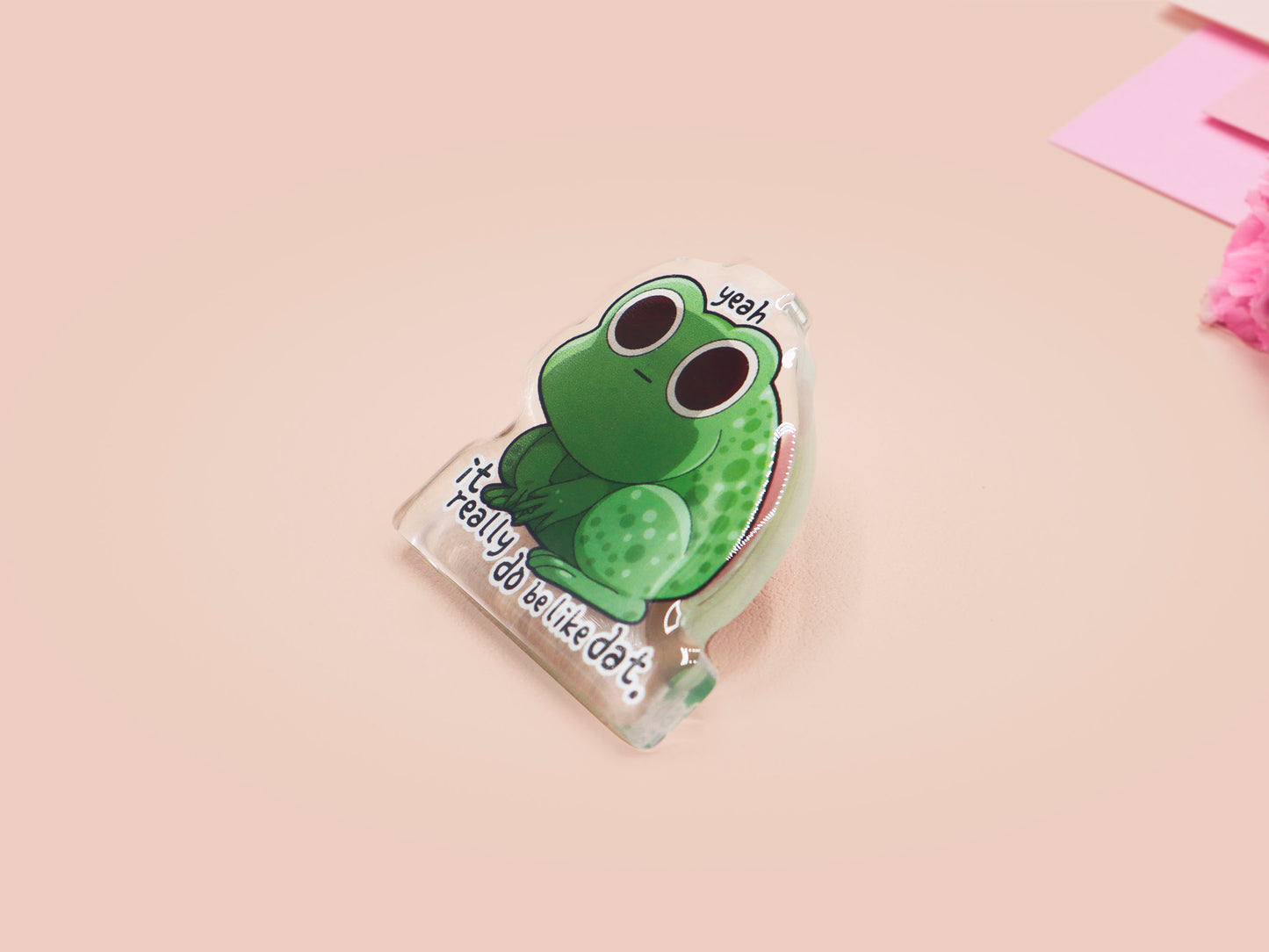 Clear acrylic pin badge with a pink heart-shaped rubber pin back clasp. The design of the pin badge is a cute cartoon stressed frog with the quote yeah it really do be like dat.