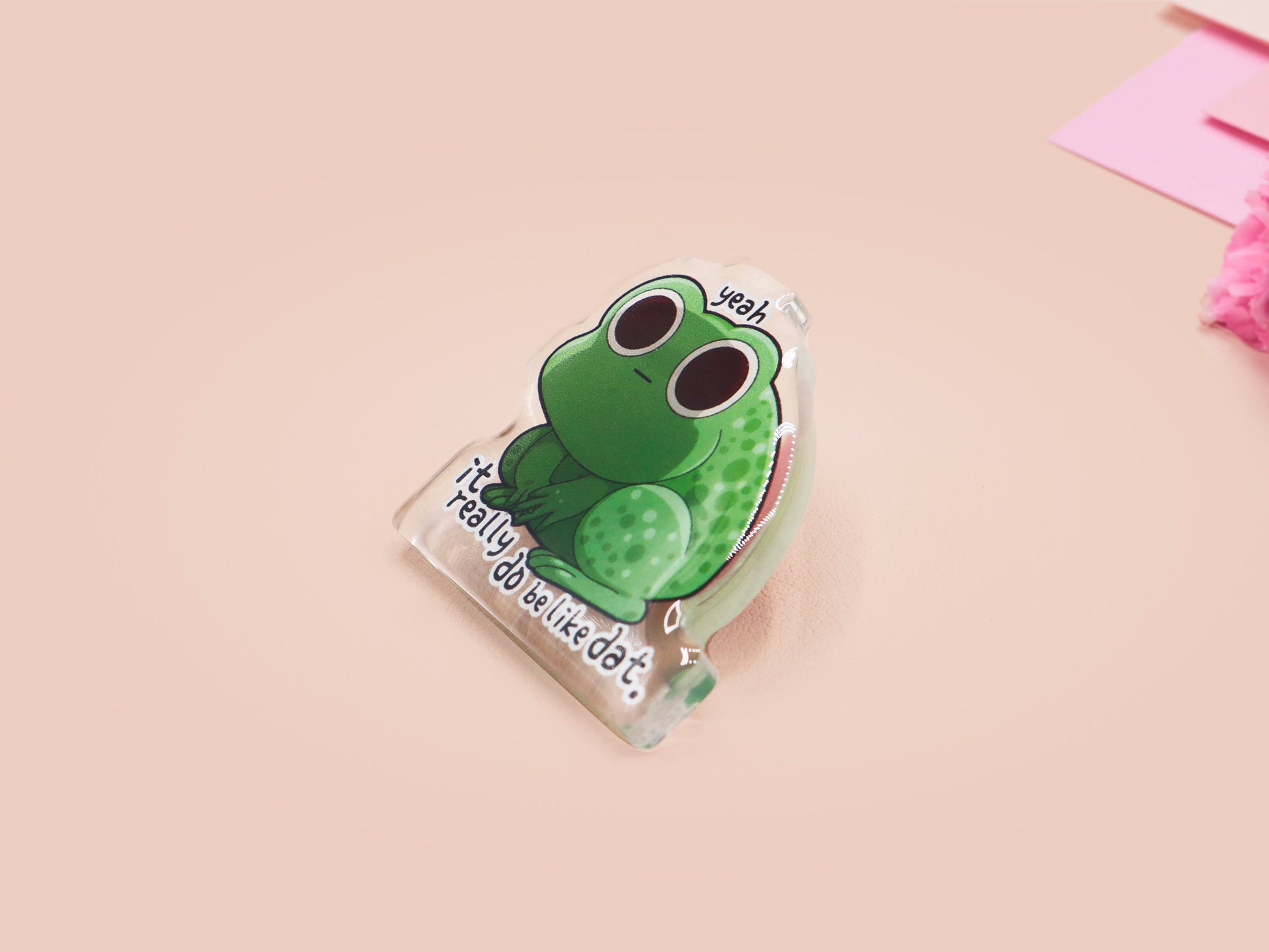 Clear acrylic pin badge with a pink heart-shaped rubber pin back clasp. The design of the pin badge is a cute cartoon stressed frog with the quote yeah it really do be like dat.